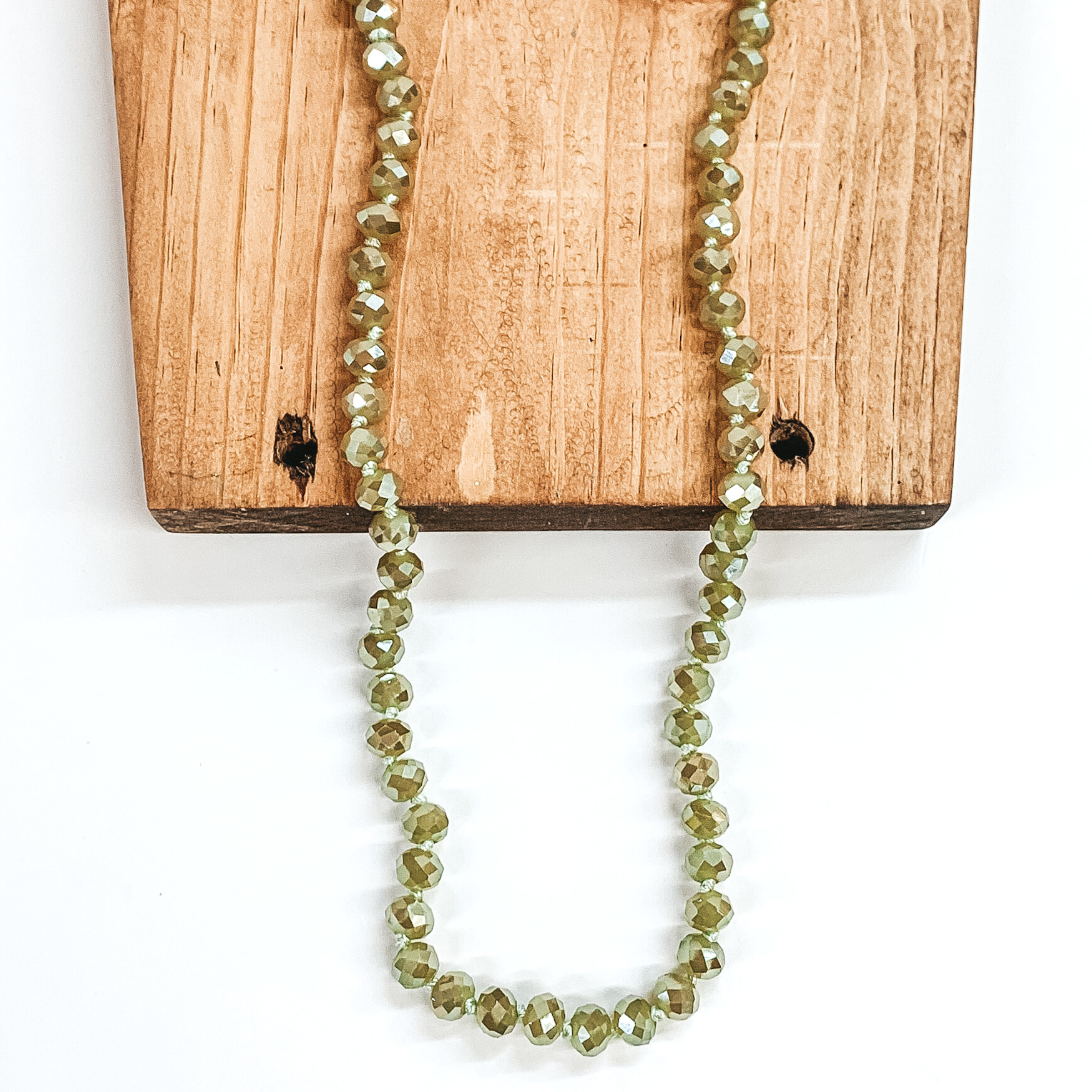 Sage green crystal beaded necklace. This necklace is pictured on a brown block on a white background. 
