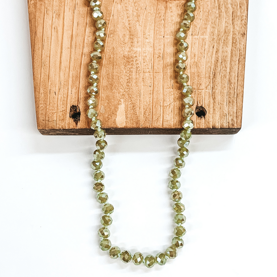 Sage green crystal beaded necklace. This necklace is pictured on a brown block on a white background. 