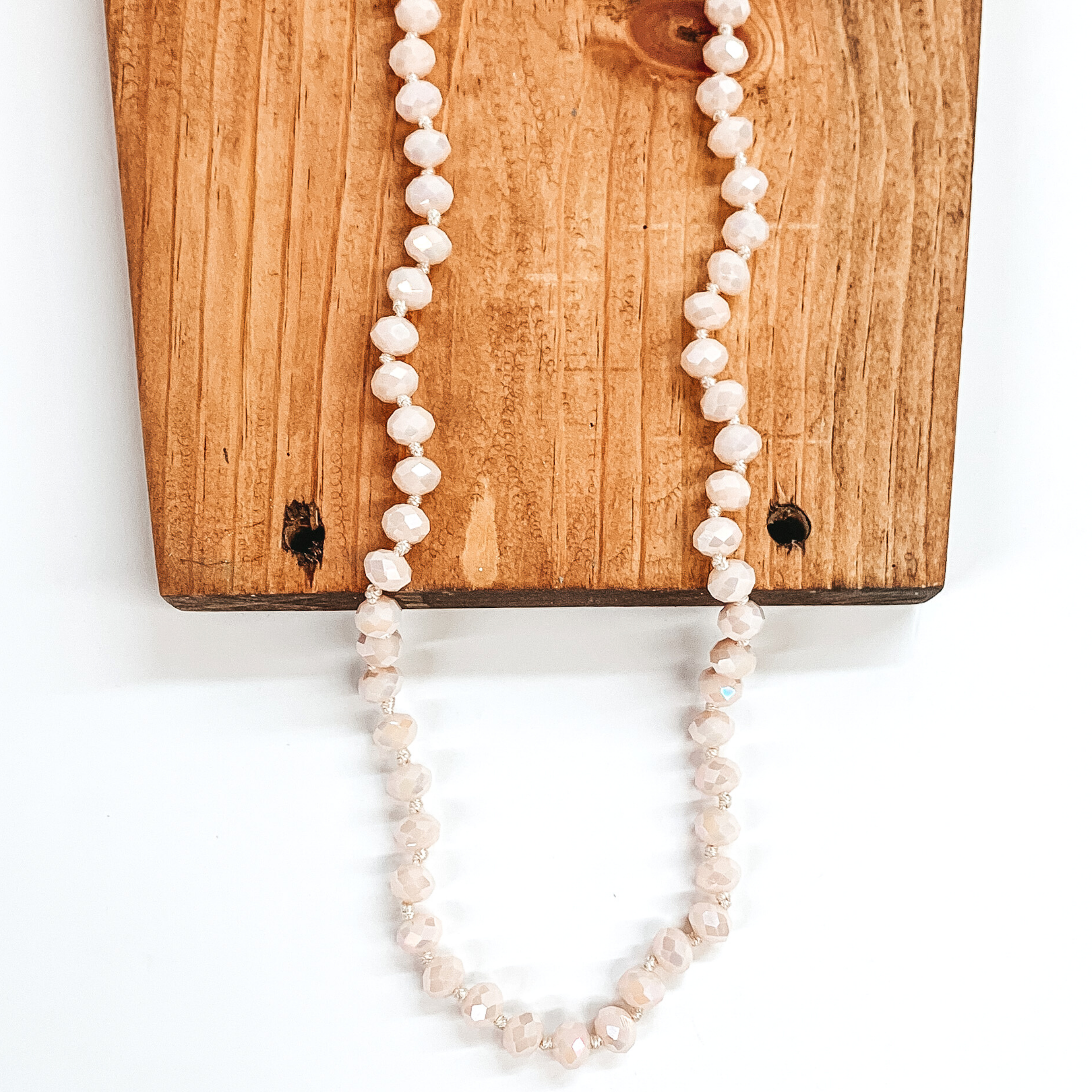 Pale pink crystal beaded necklace. This necklace is pictured partially laying on a brown block on a white background. 