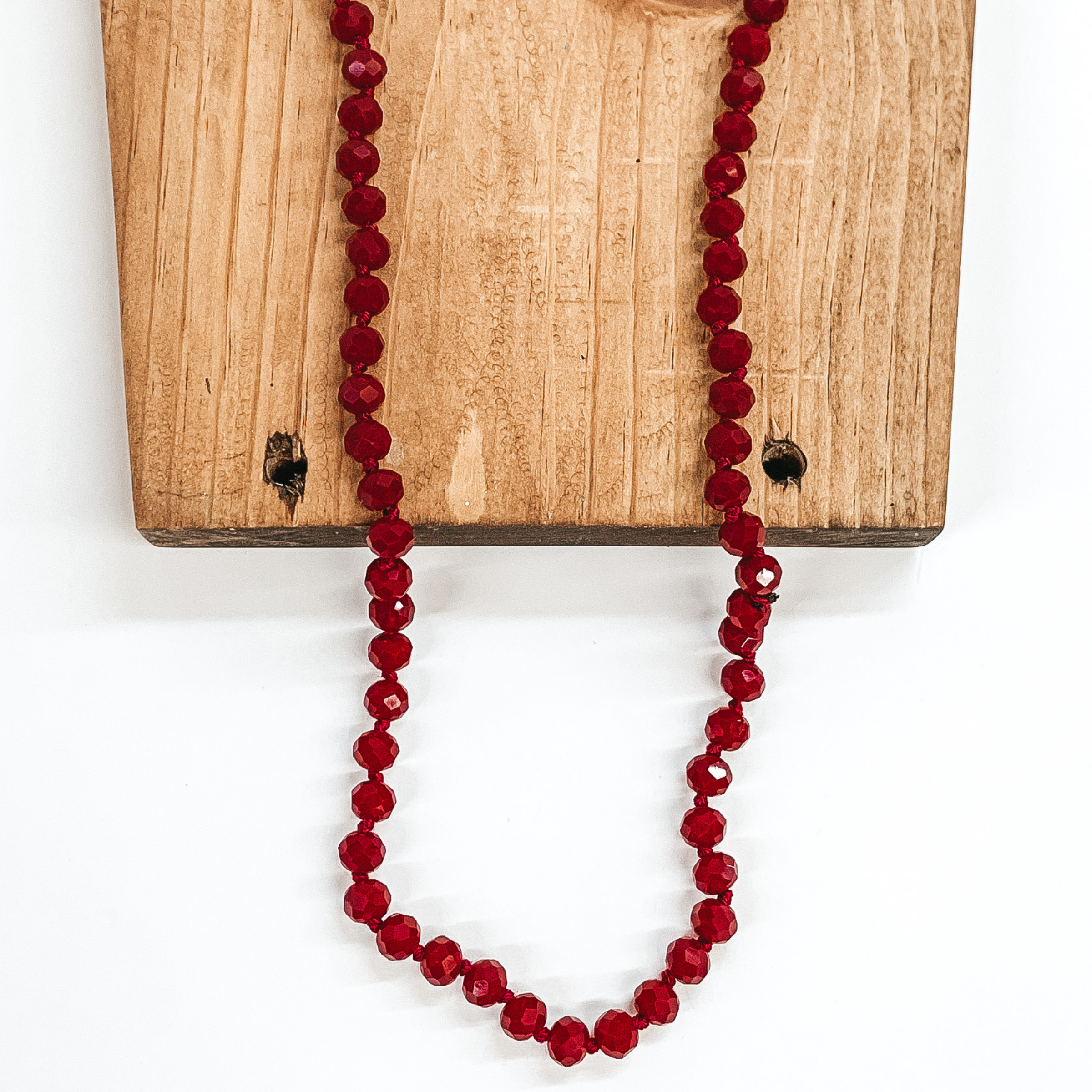 Red velvet crystal beaded necklace. This necklace is pictured partially laying on brown block on a white background. 