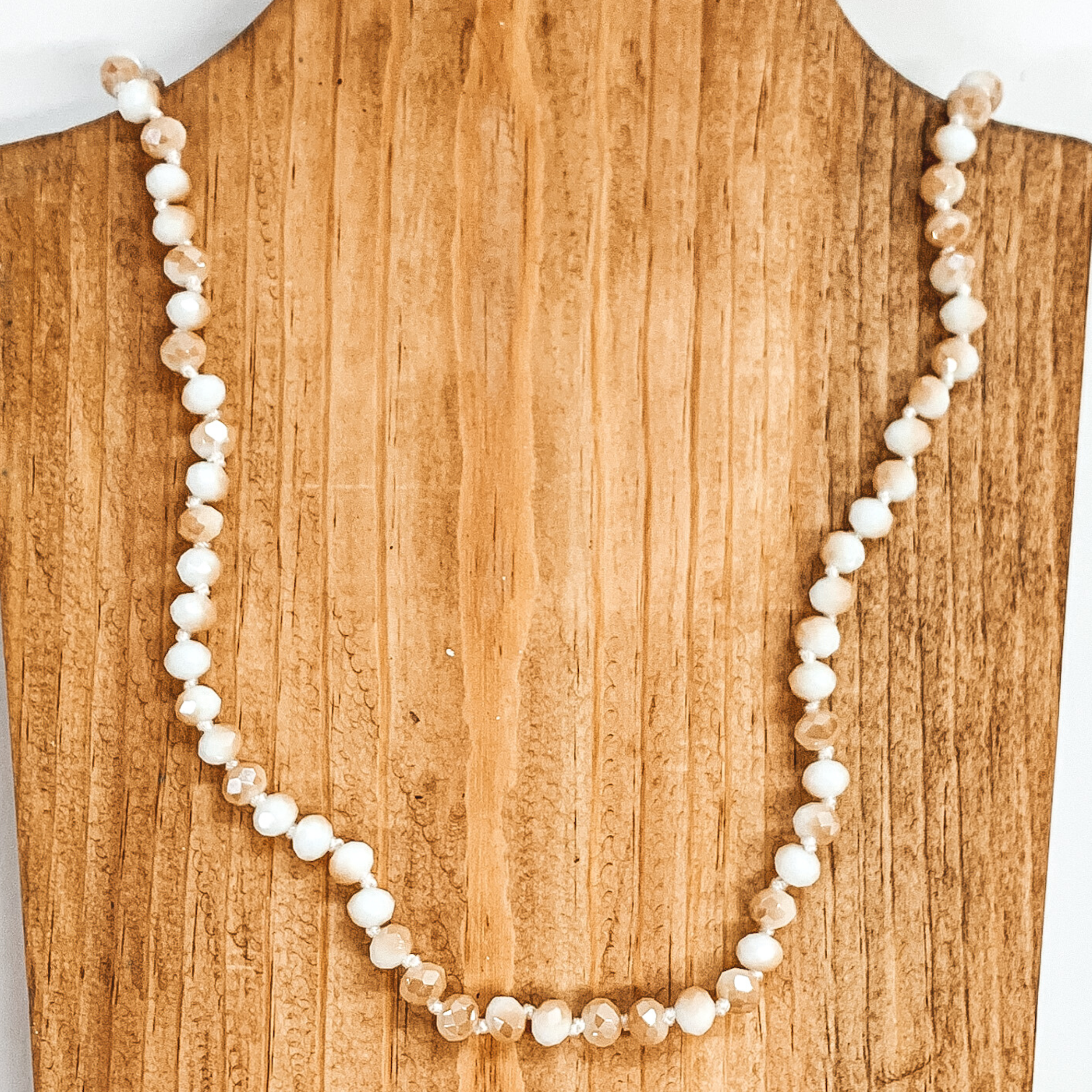 White and tan crystal beaded necklace. This necklace is pictured on a brown necklace holder on a white background. 
