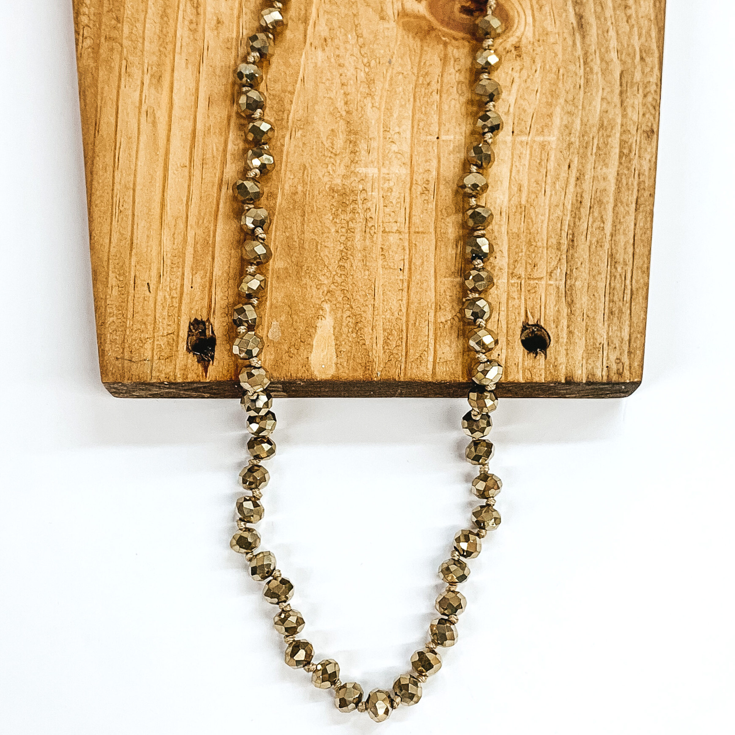 Yellowish gold crystal beaded necklace. This necklace is pictured partially laying on a brown block on a white background. 