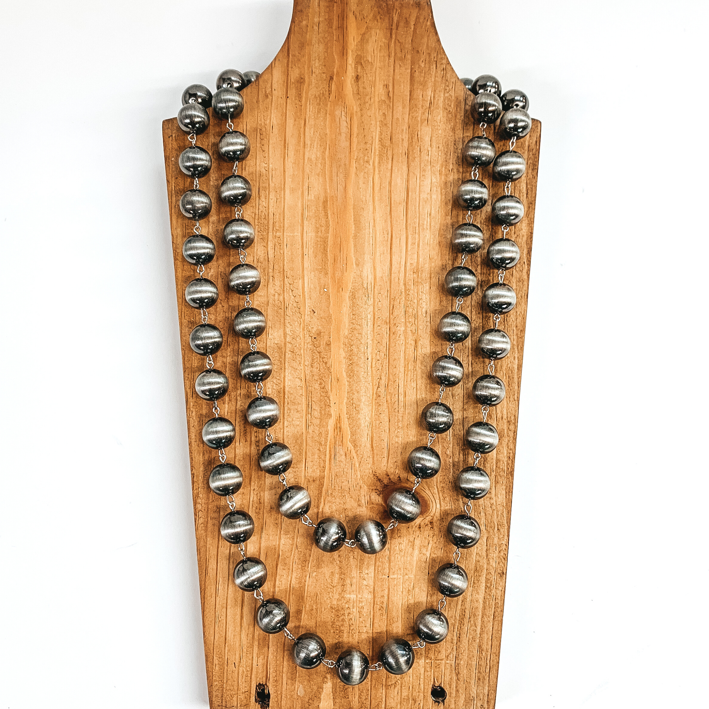 Silver beaded necklace that is connected by silver rings. This necklace is pictured on a brown necklace holder on a white background. 
