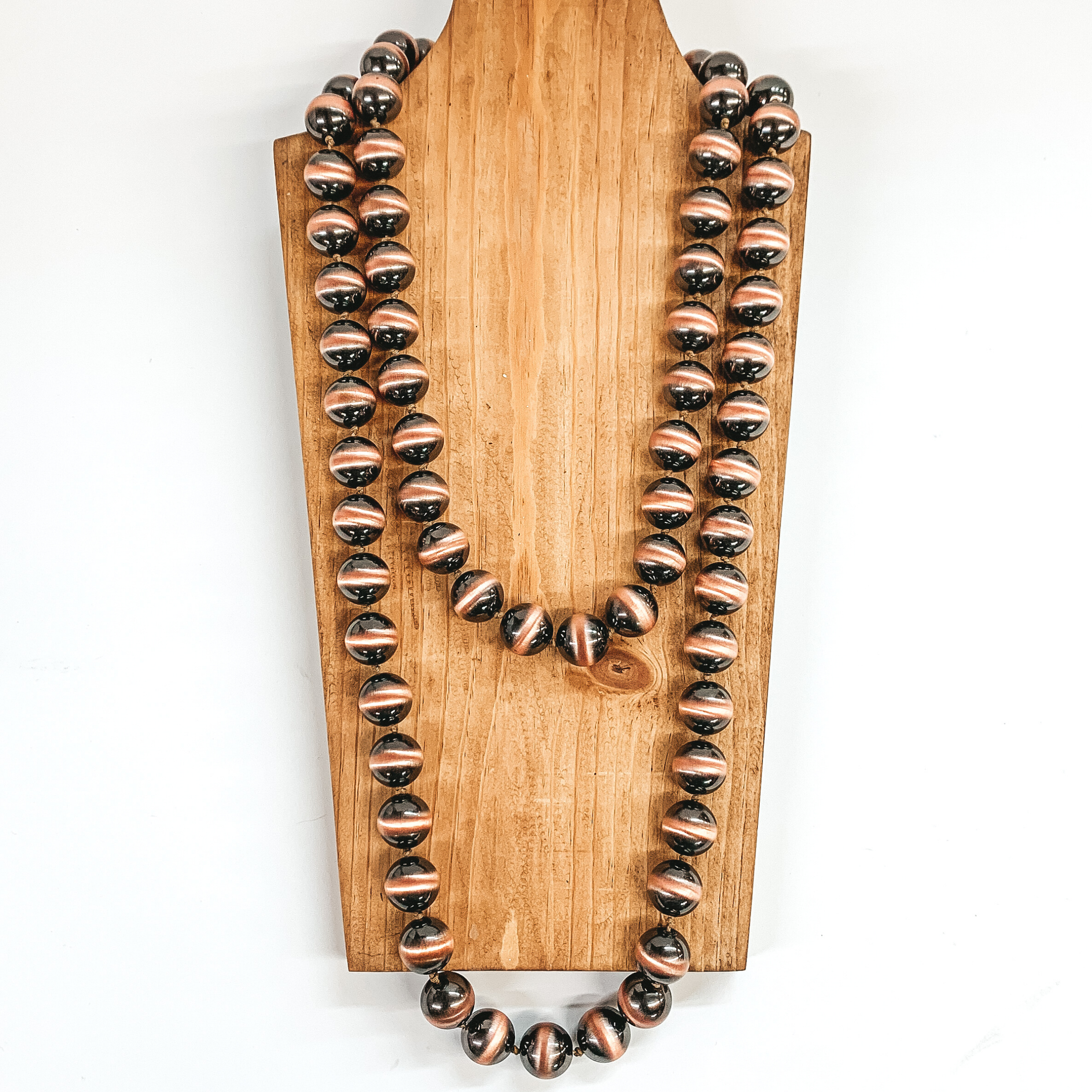 Copper beaded necklace that is pictured on a brown necklace holder on a white background.