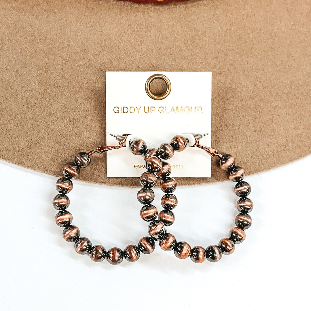 Copper beaded hoop earrings. These earrings are pictured on a tan and white background.