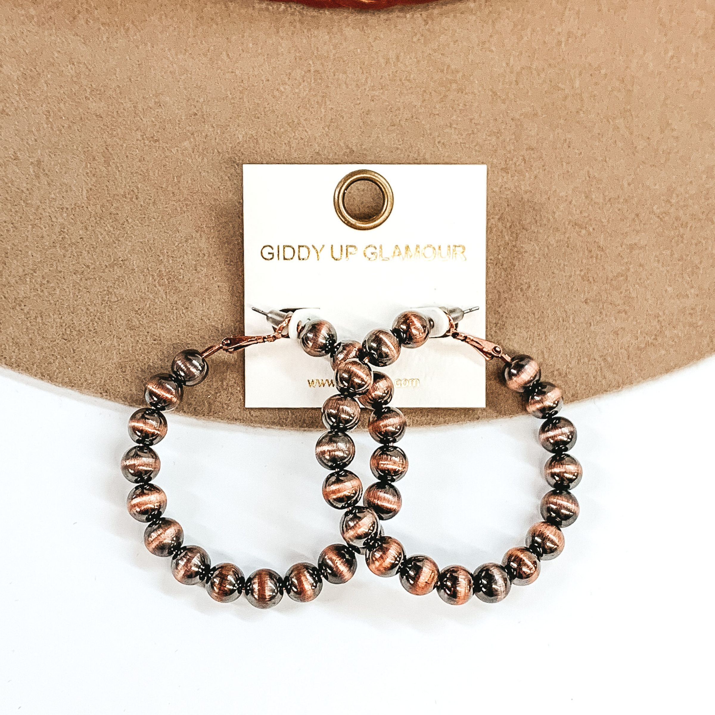 Copper beaded hoop earrings. These earrings are pictured on a tan and white background.