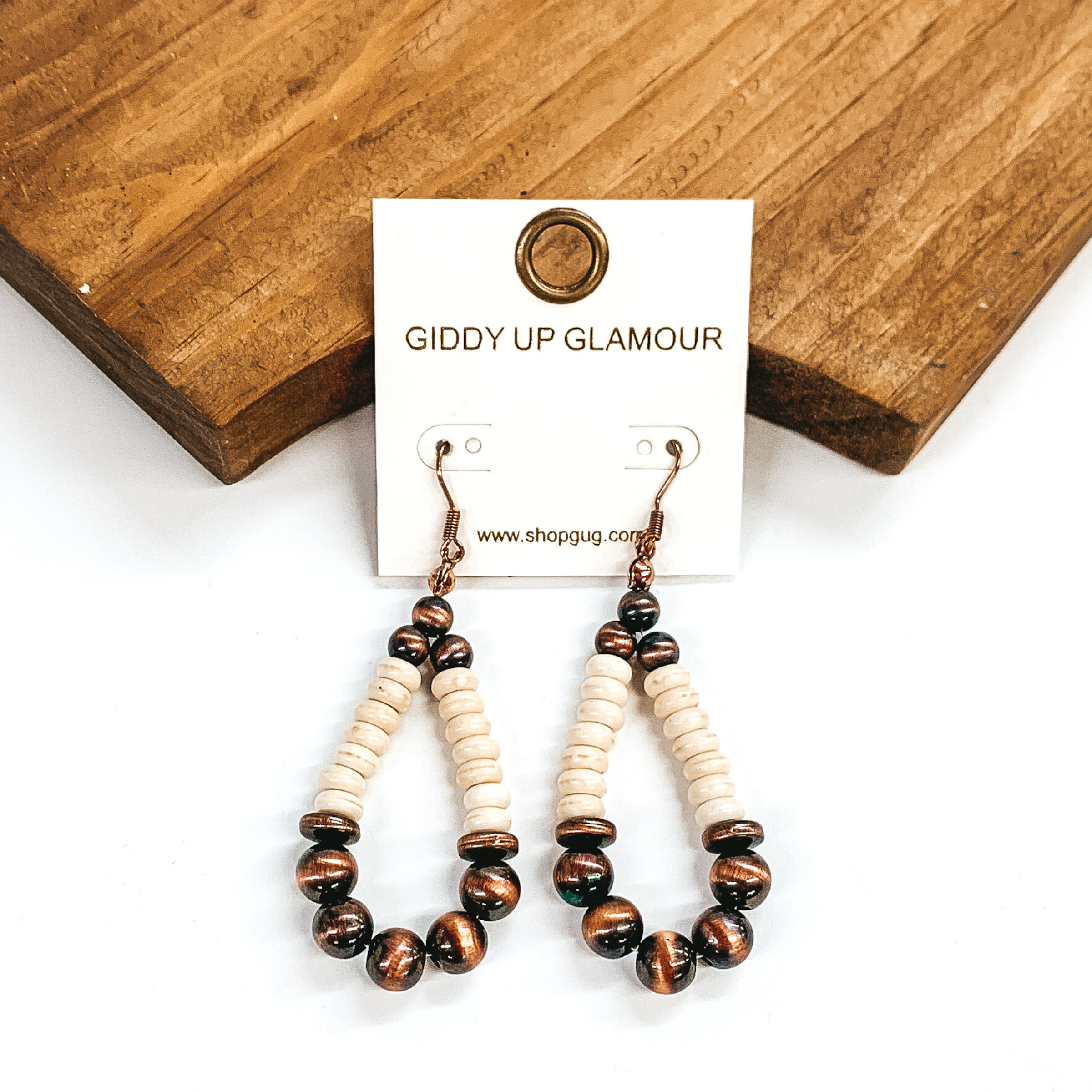 Teardrop beaded earrings. These earrings have a bottom and top section of copper beads that are separted by ivory beaded segments. These earrings are pictured in front of a brown block on a white background. 