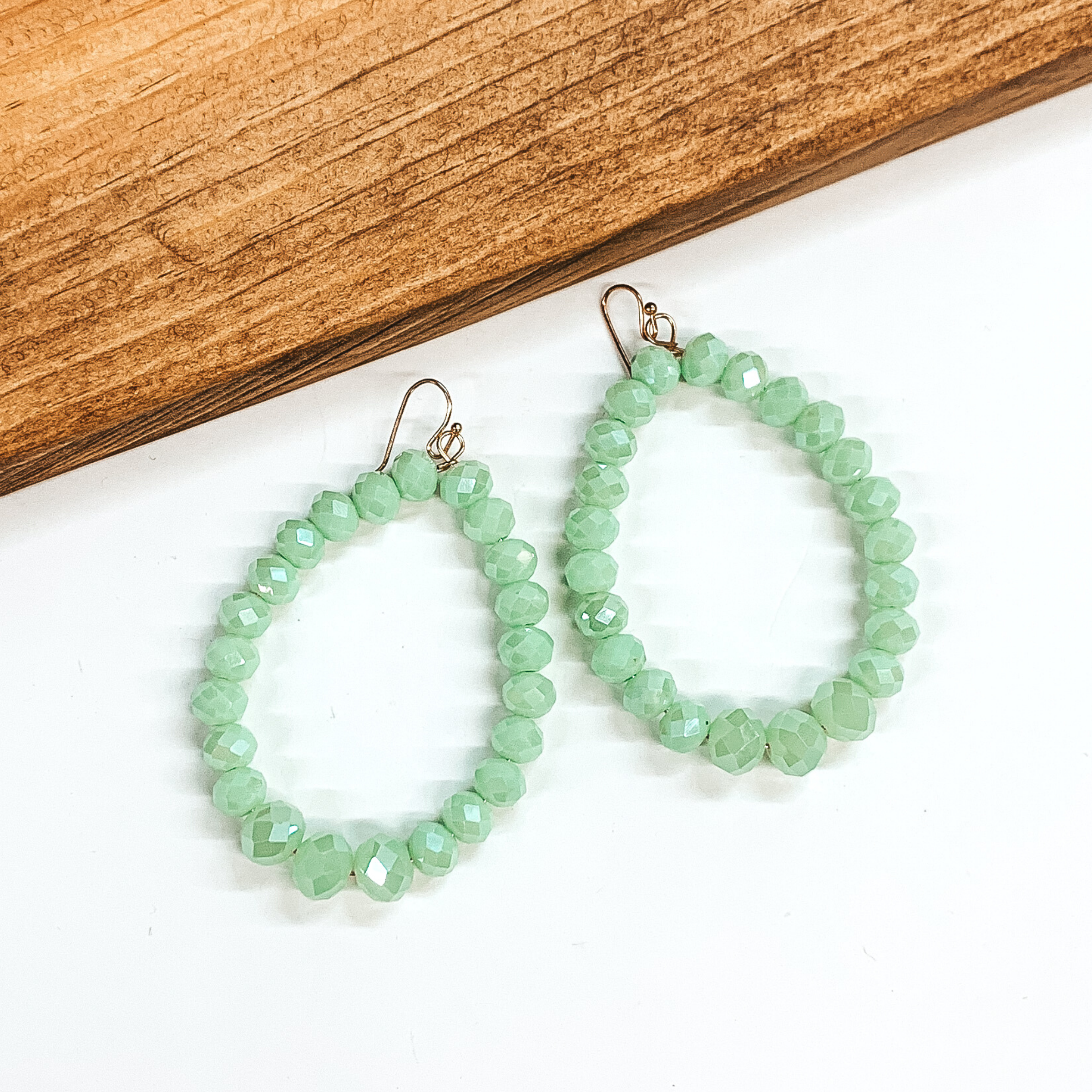 Crystal beaded open teardrop earrings in mint. These earrings are pictured on a white background with a brown block at the top left corner.