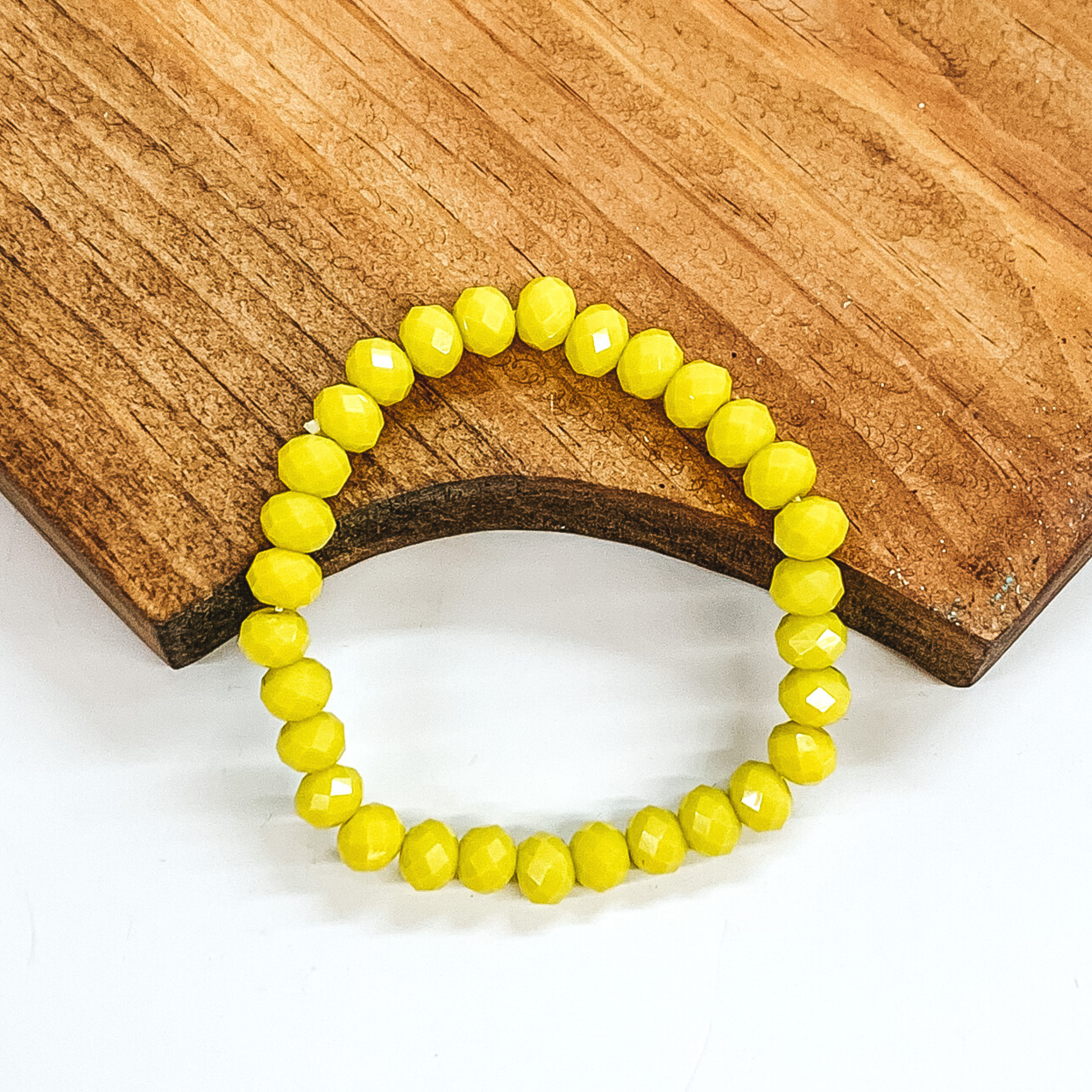 Crystal beaded bracelet in yellow. These earrings are pictured on a partially laying on a brown block on a white background.