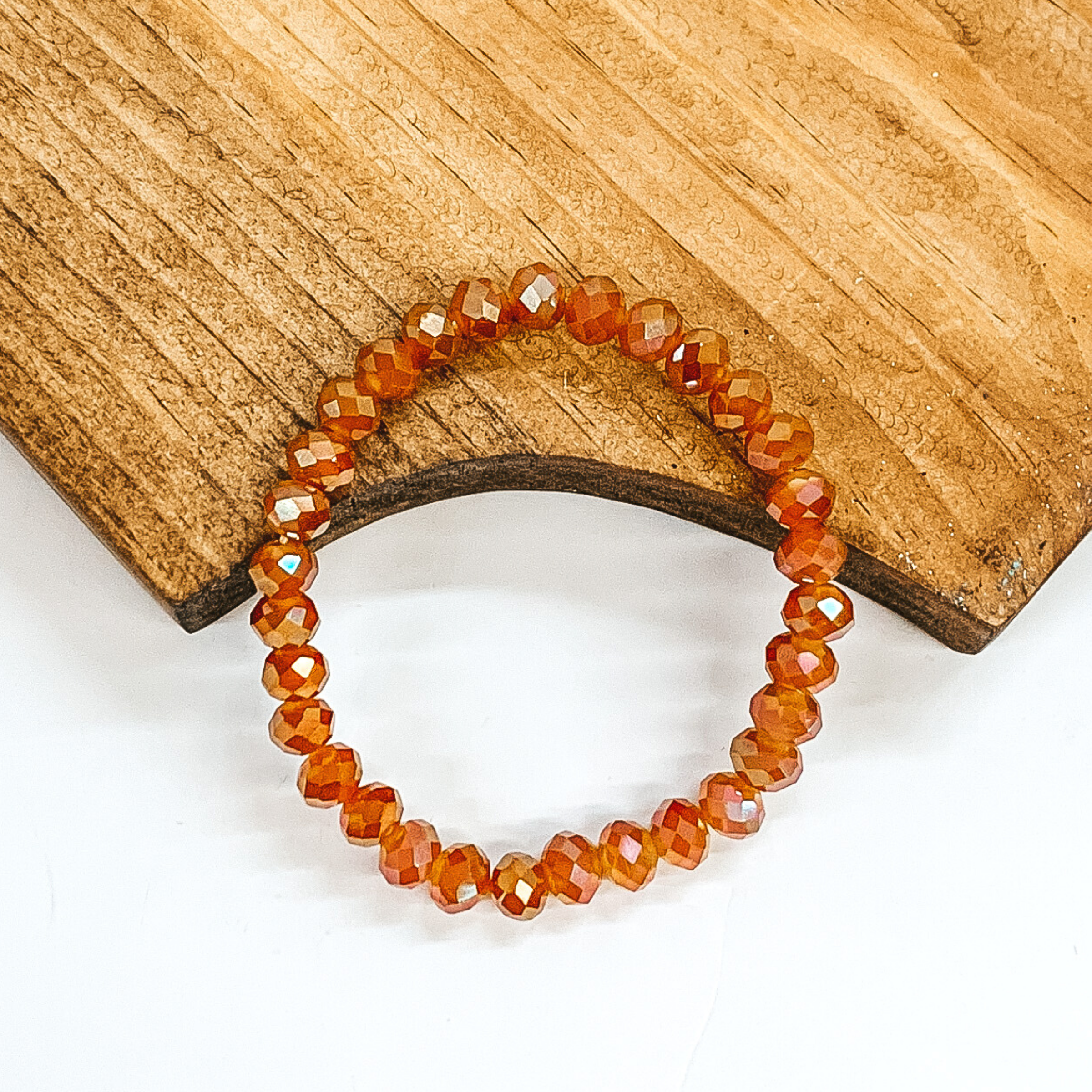 Crystal beaded bracelet in rust orange. This bracelet is pictured on a partially laying on a brown block on a white background.