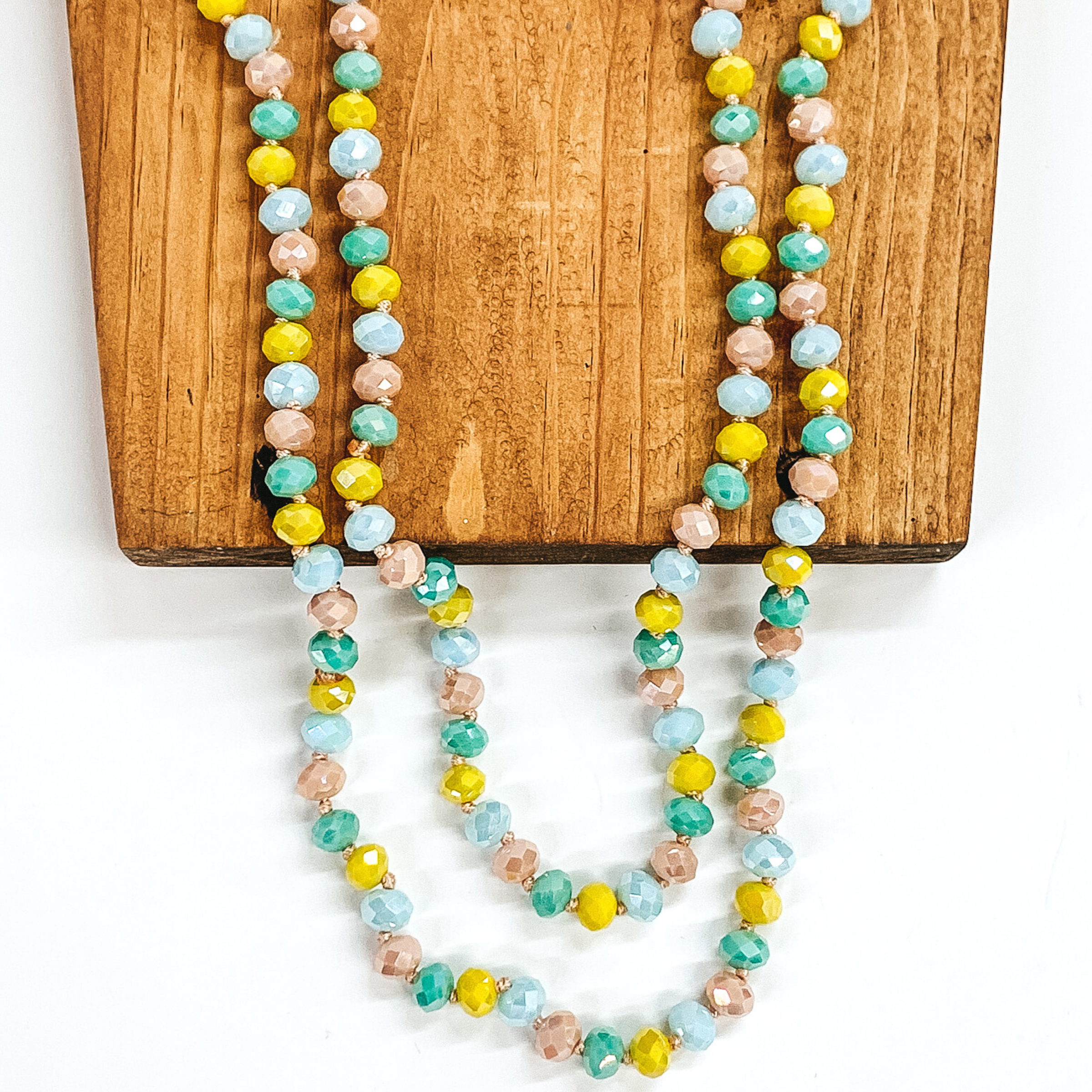 Crystal beaded necklace in green, blue, yellow, and taupe. This necklace is pictured on a wooden necklace holder on a white background. 