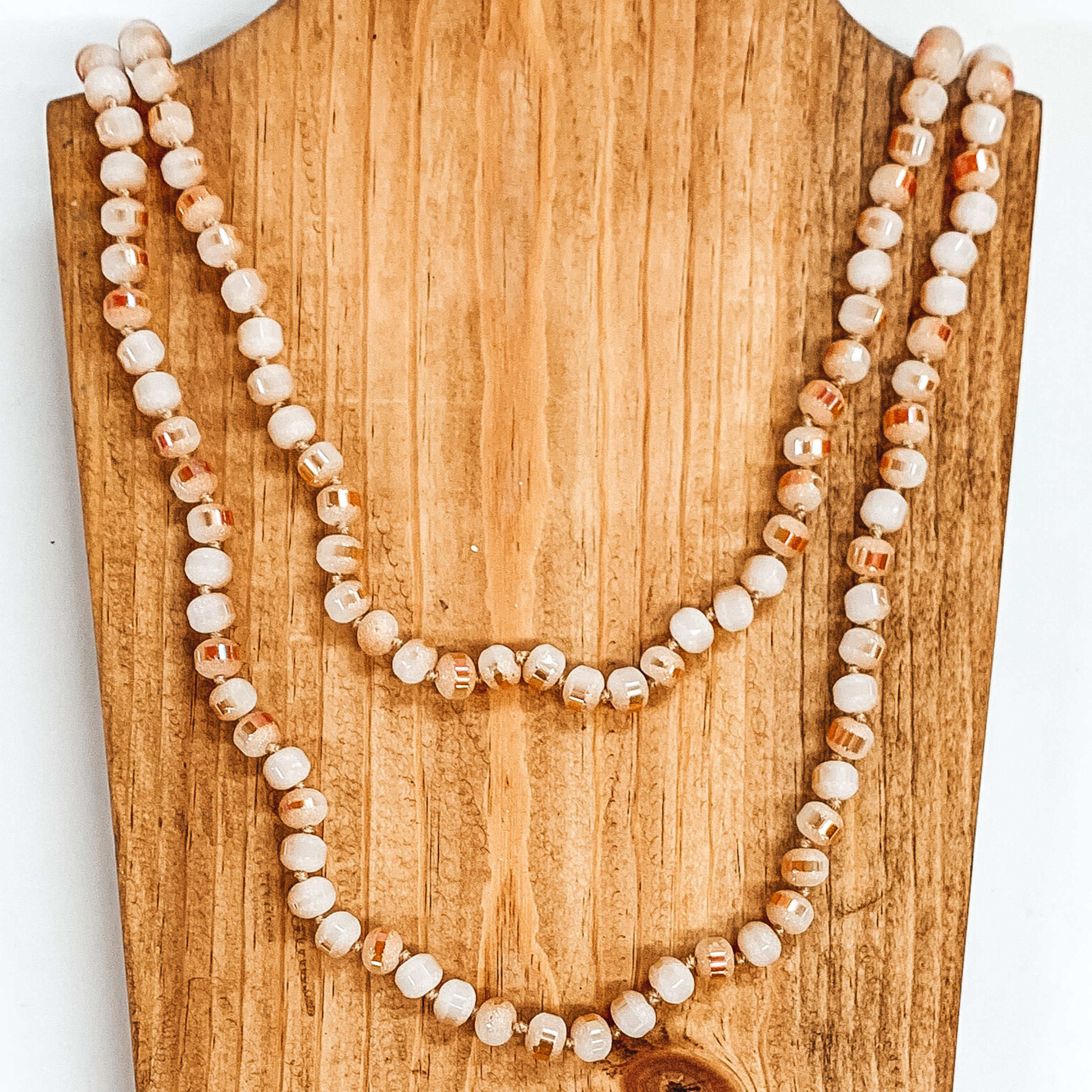  Crystal beaded necklace in druzy blush and ivory. This necklace is pictured laying on a brown necklace holder on a white background.