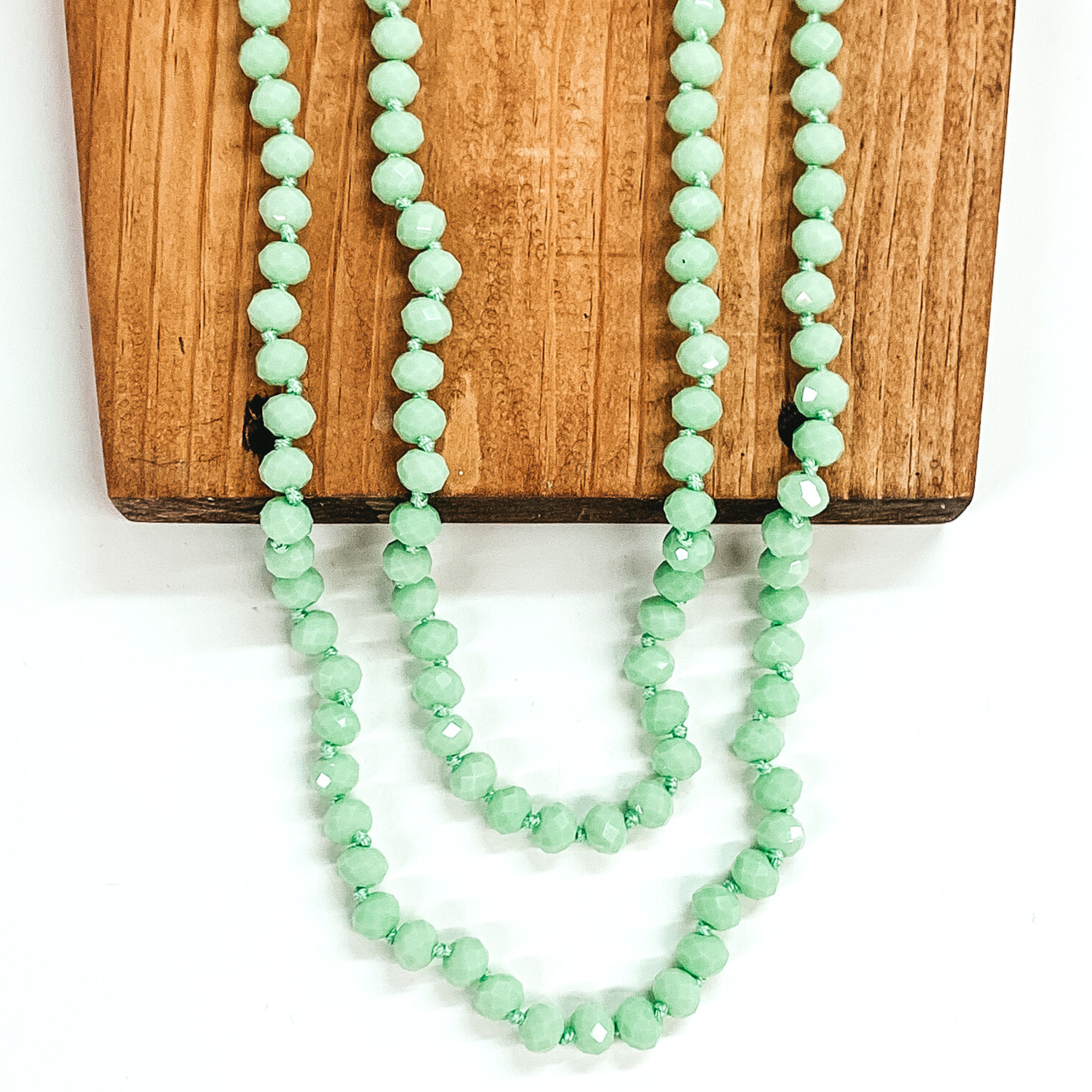 Crystal beaded necklace in mint. This necklace is pictured laying on a brown block on a white background.
