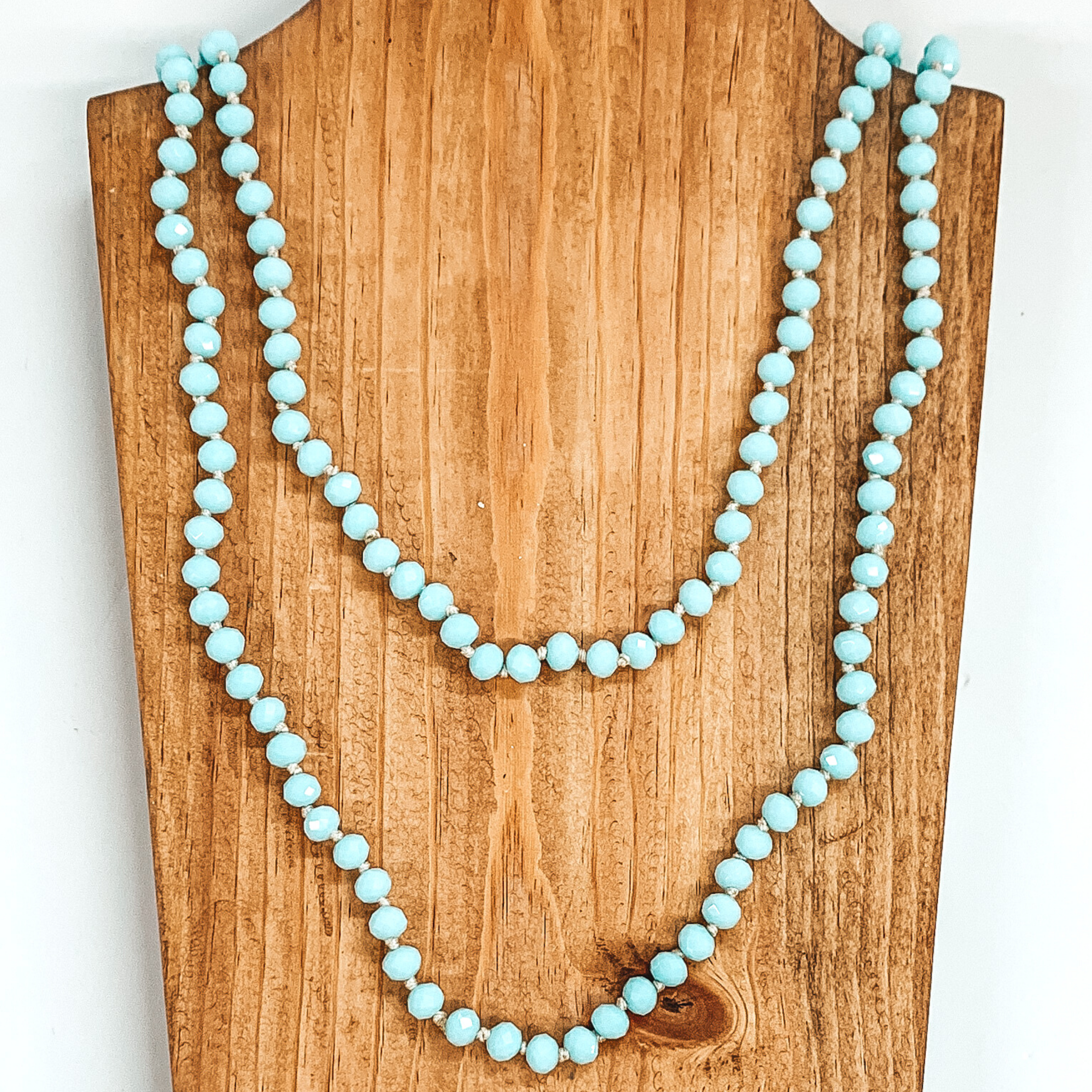 Crystal beaded necklace in pastel blue. This necklace is pictured laying on a brown necklace holder on a white background.