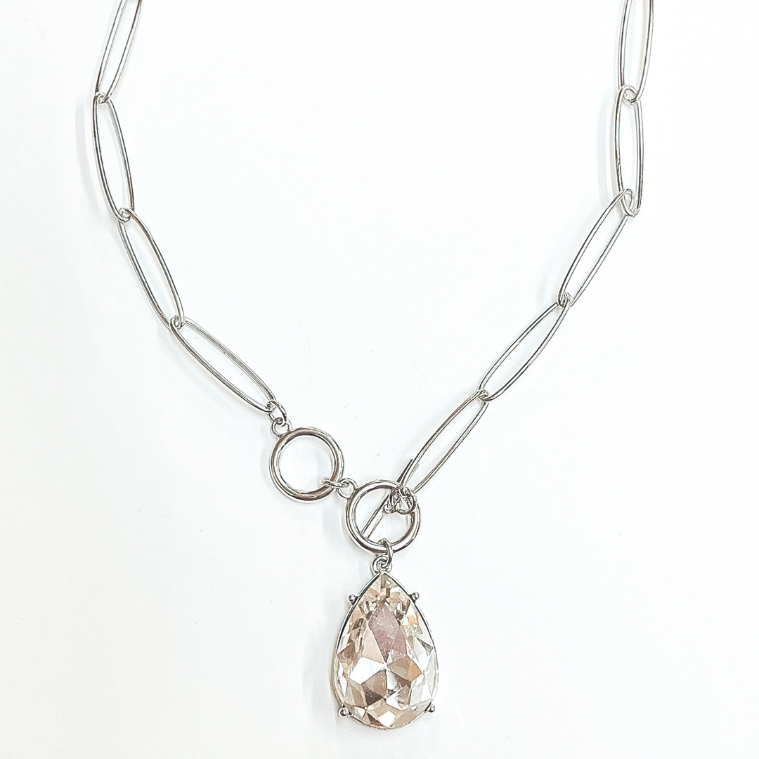Silver, thin chain necklace with front toggle clasp. This necklace includes a clear teardrop crystal. This necklace is pictured on a white background. 