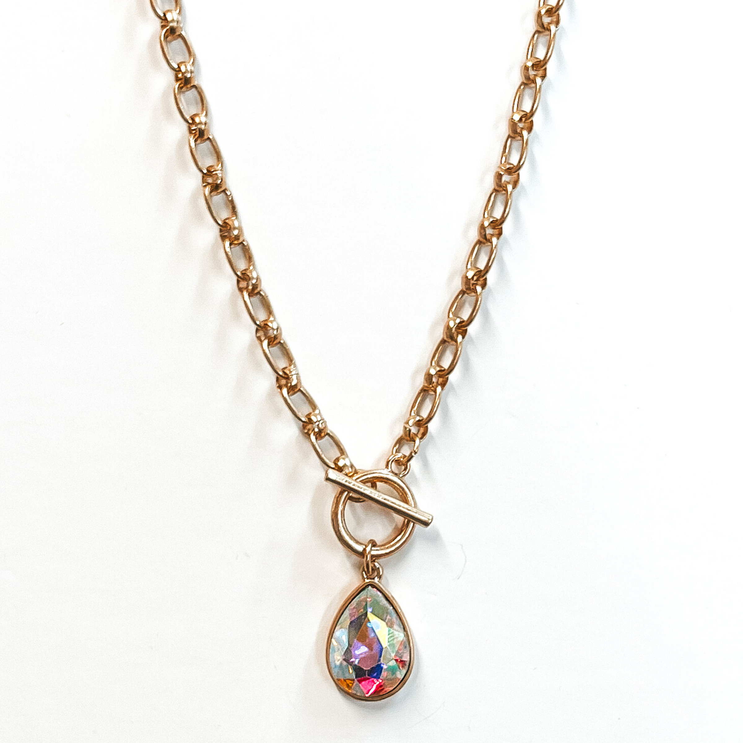 Gold chain necklace with front toggle clasp. This necklace includes an AB teardrop crystal with a gold backing. This necklace is pictured on a white background. 
