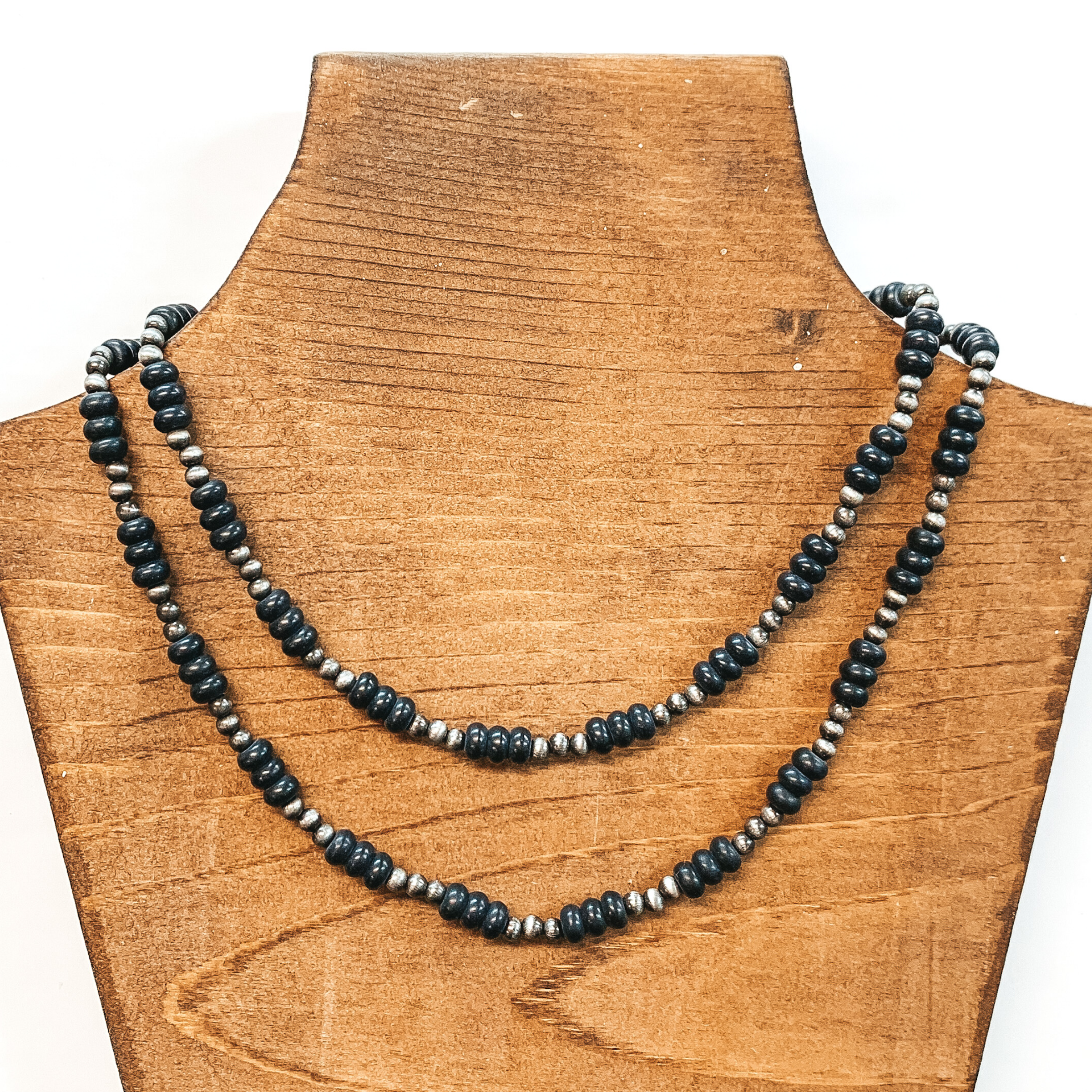 Two strand necklace that includes silver bead segments with bigger, black bead segments. This necklace is pictured on a brown necklace holder on a white background.