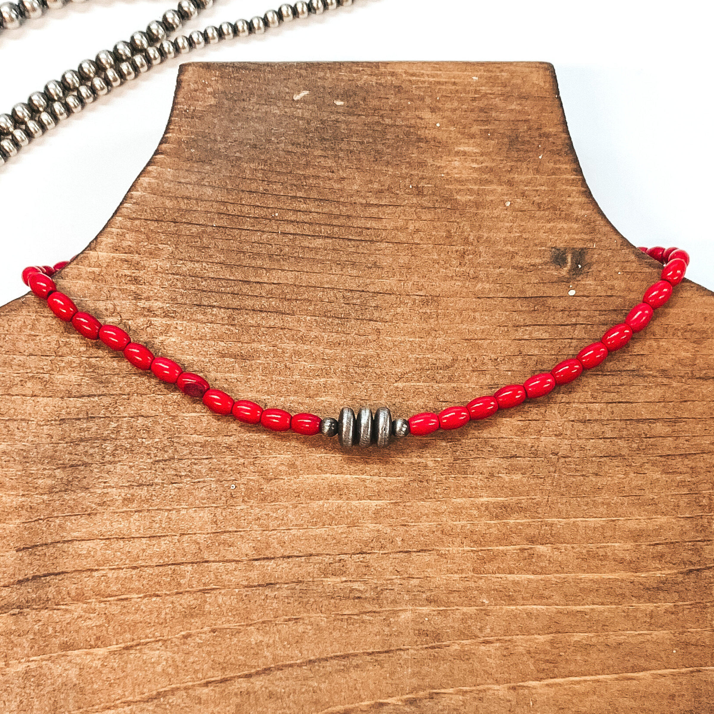 Red beaded necklace with silver, saucer beads in the center. This necklace is pictured on a brown necklace holder on a white background with silver beads in the background.