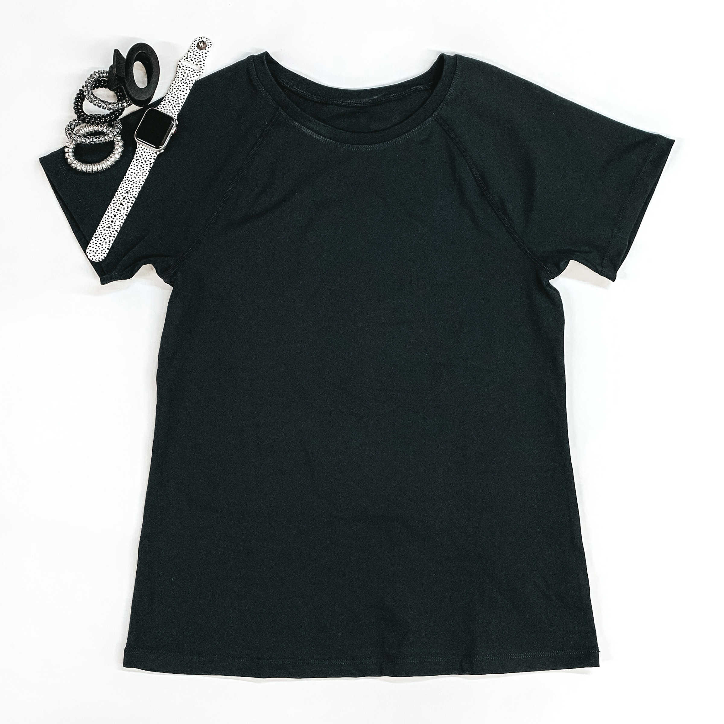 Black shorts sleeve top pictured on a white background with hair ties, a black clip, and a smart watch at the top left corner.