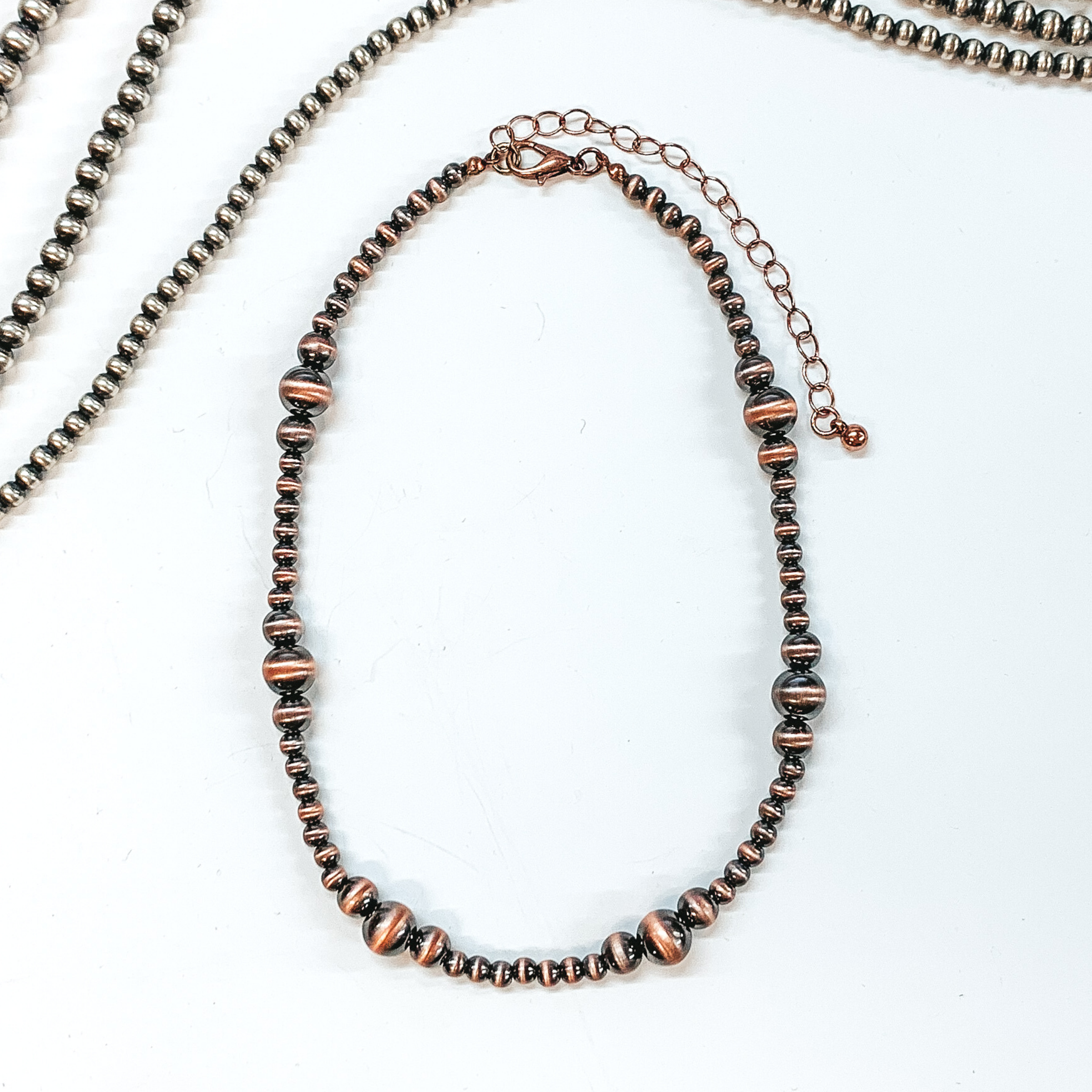 Copper colored bead necklace with larger bead spacers throughout. This necklace is pictured on a white background with silver beads at the top of the picture. 