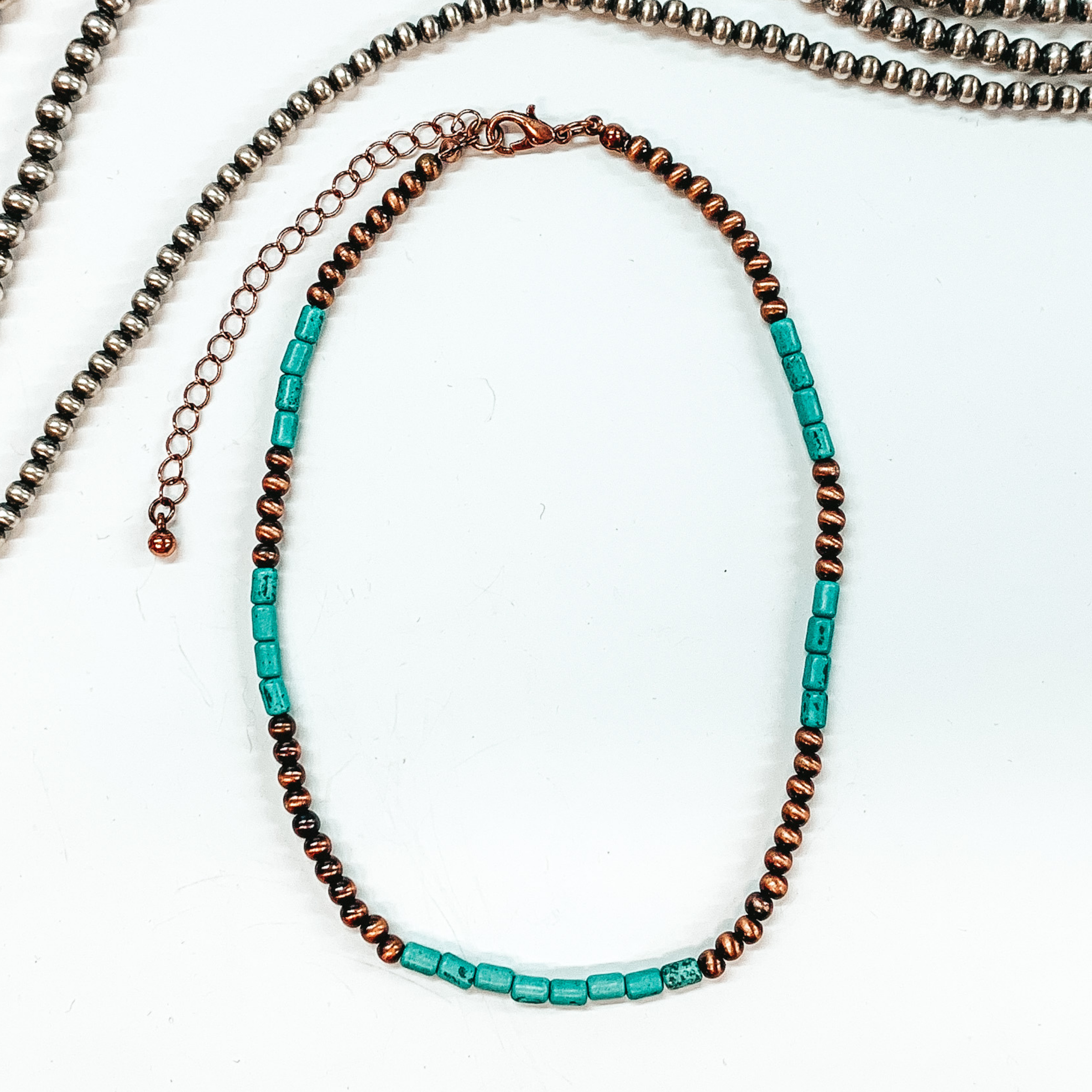 Round copper beads and cylinder turquoise beads. This necklace is pictured laying on a white background with silver beads at the top of the picture. 