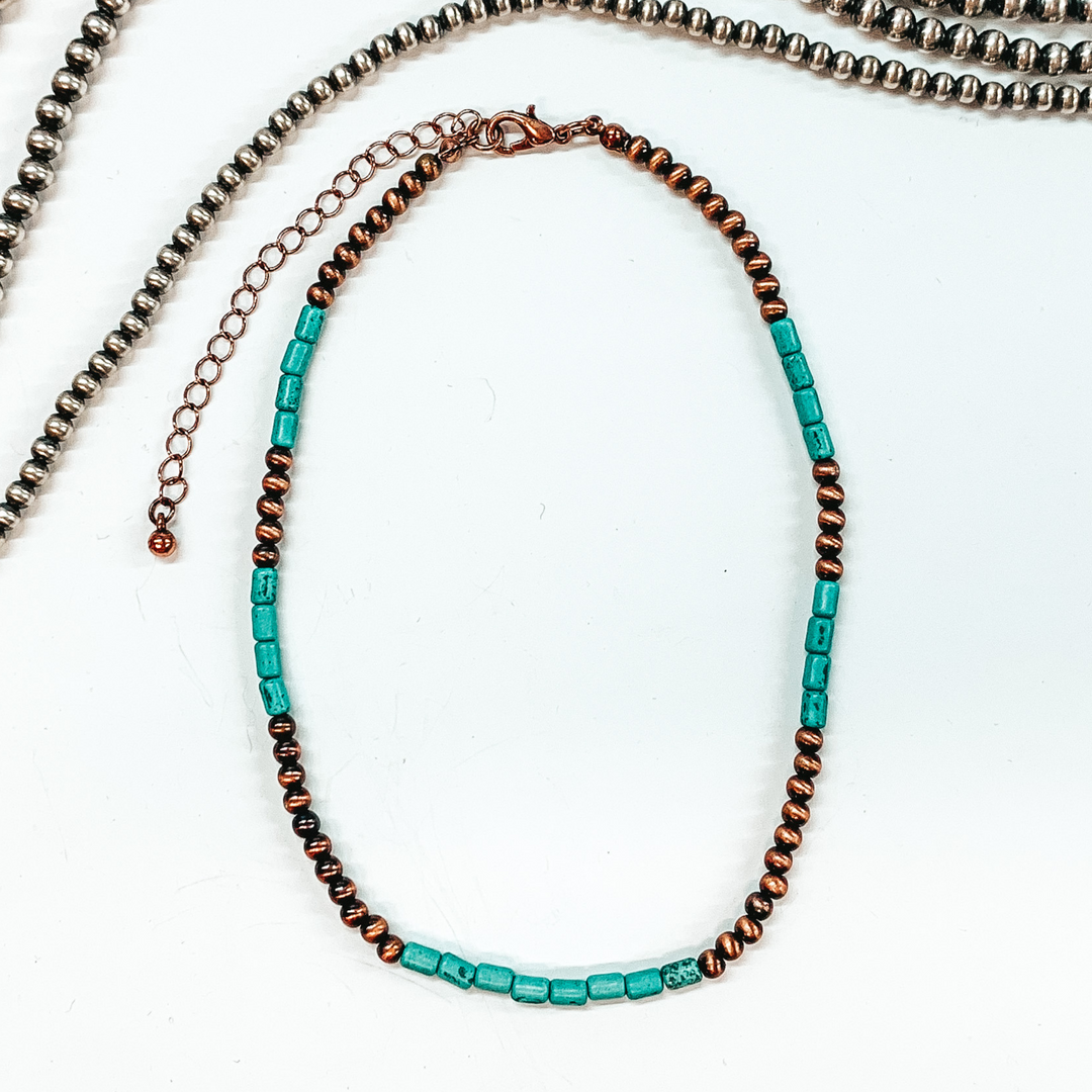 Round copper beads and cylinder turquoise beads. This necklace is pictured laying on a white background with silver beads at the top of the picture. 