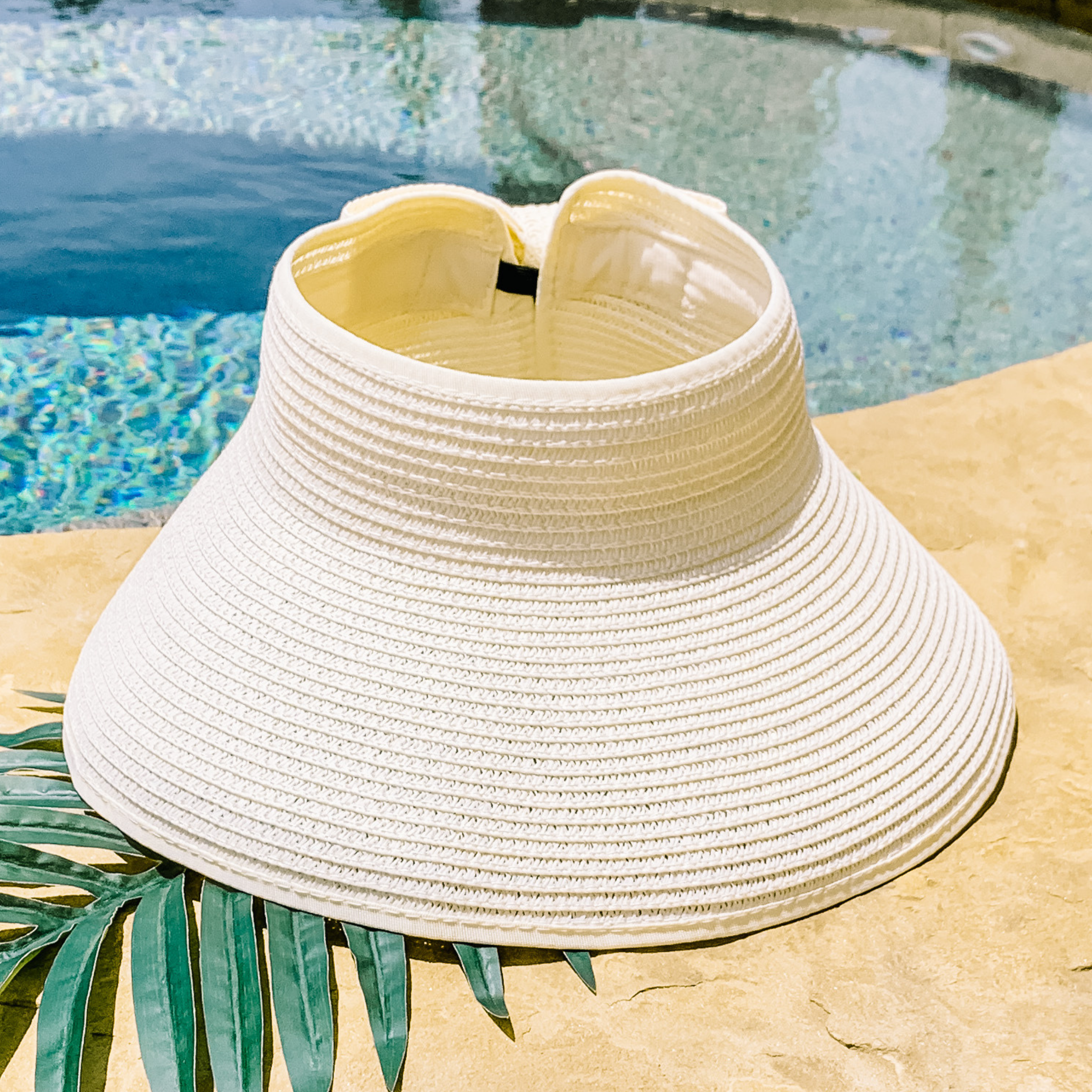 Ivory, woven velcro visor that is pictured with a green leaf under it. This visor is pictured on a a tan rock in front of a pool.