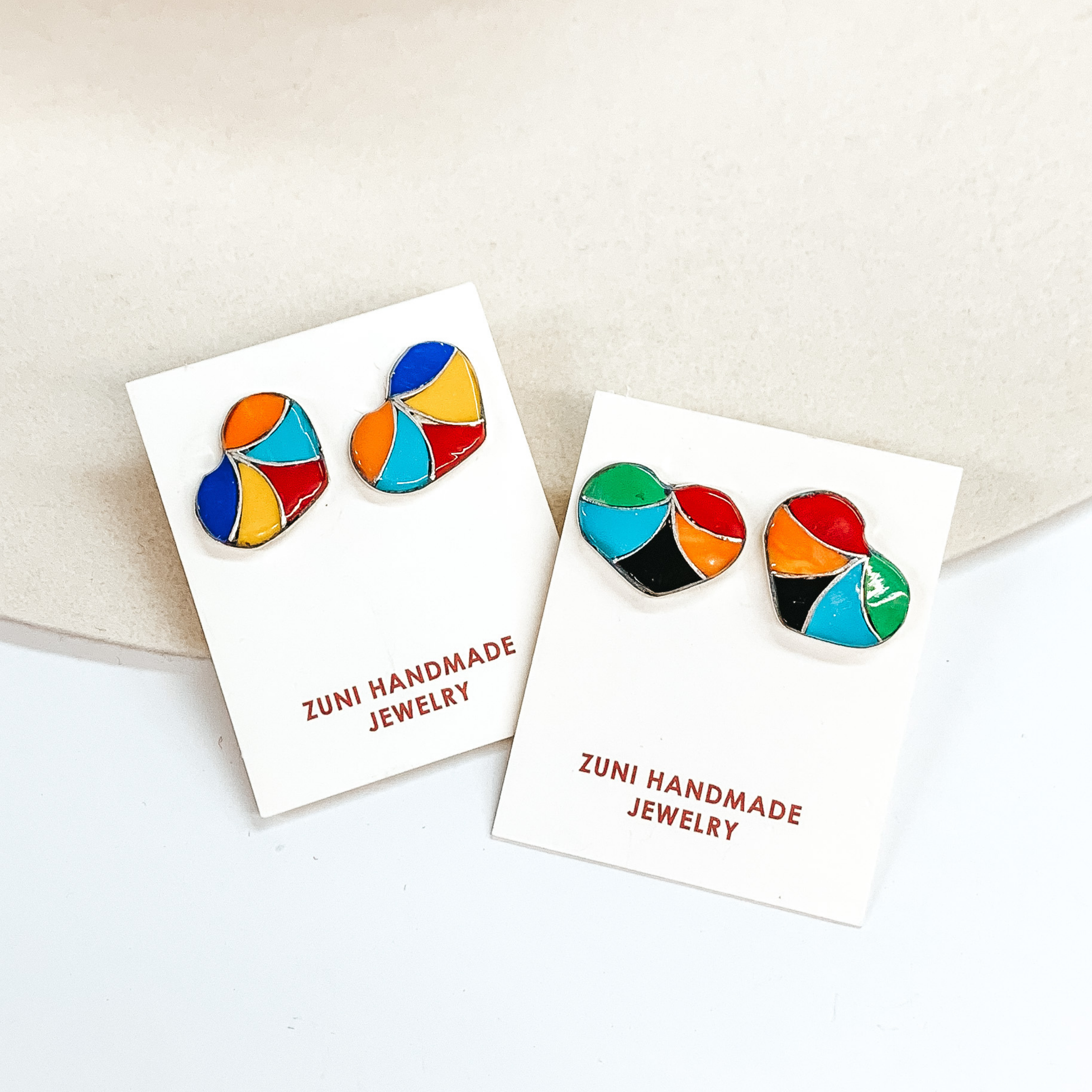 Silver heart studs with color blocking inlay. These earrings are pictured on a white cardstock on a white background. 