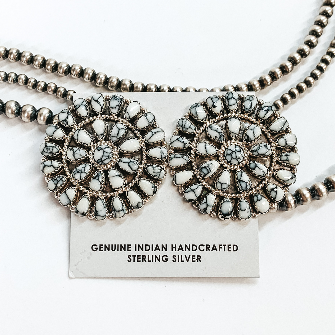 Silver, circle white buffalo stone cluster. These earrings are pictured on a white cardstock on a white background with silver beads behind the earrings. 