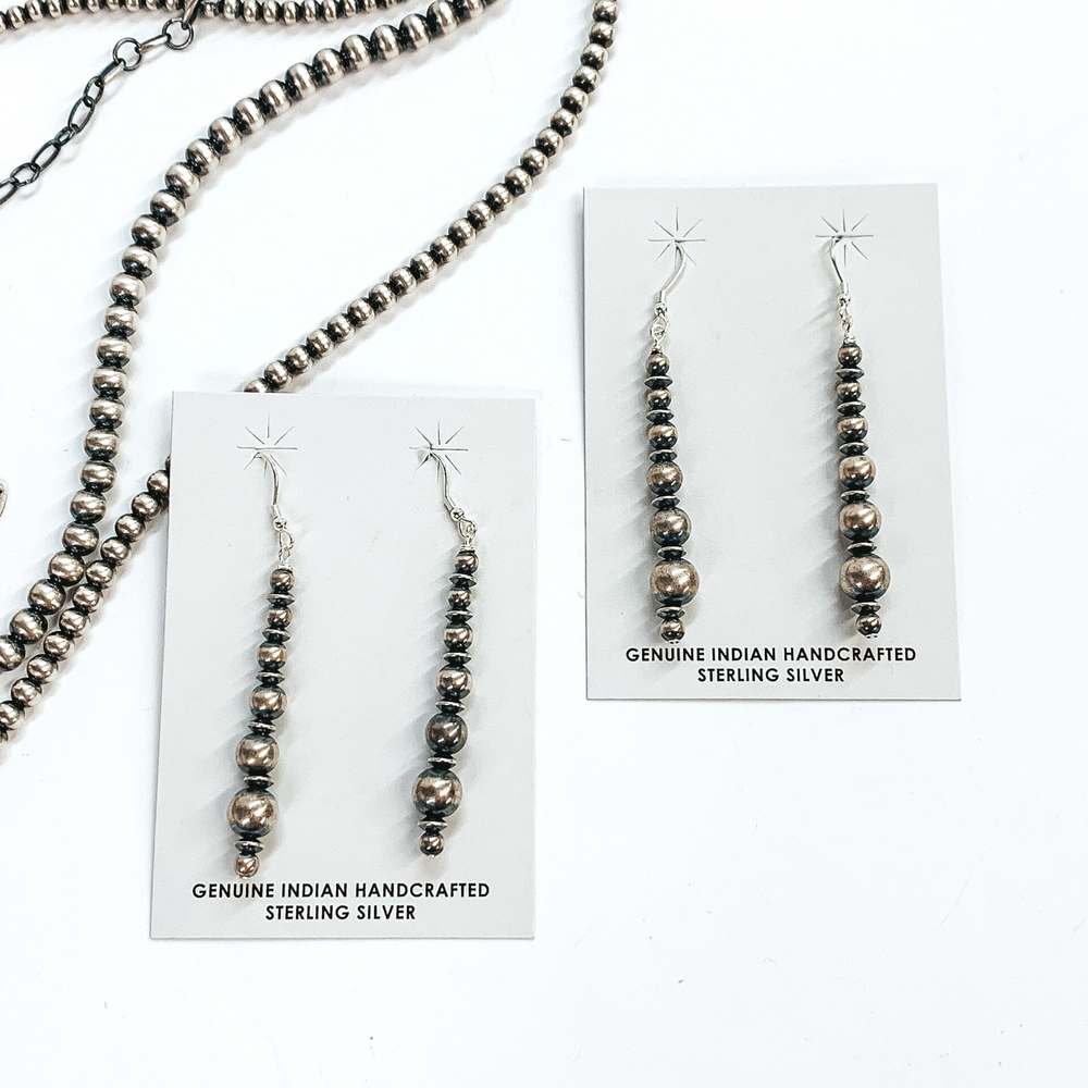 Silver, graduated beads and saucer beaded drop earrings. These earrings are pictured on a white background on top of silver beads. 