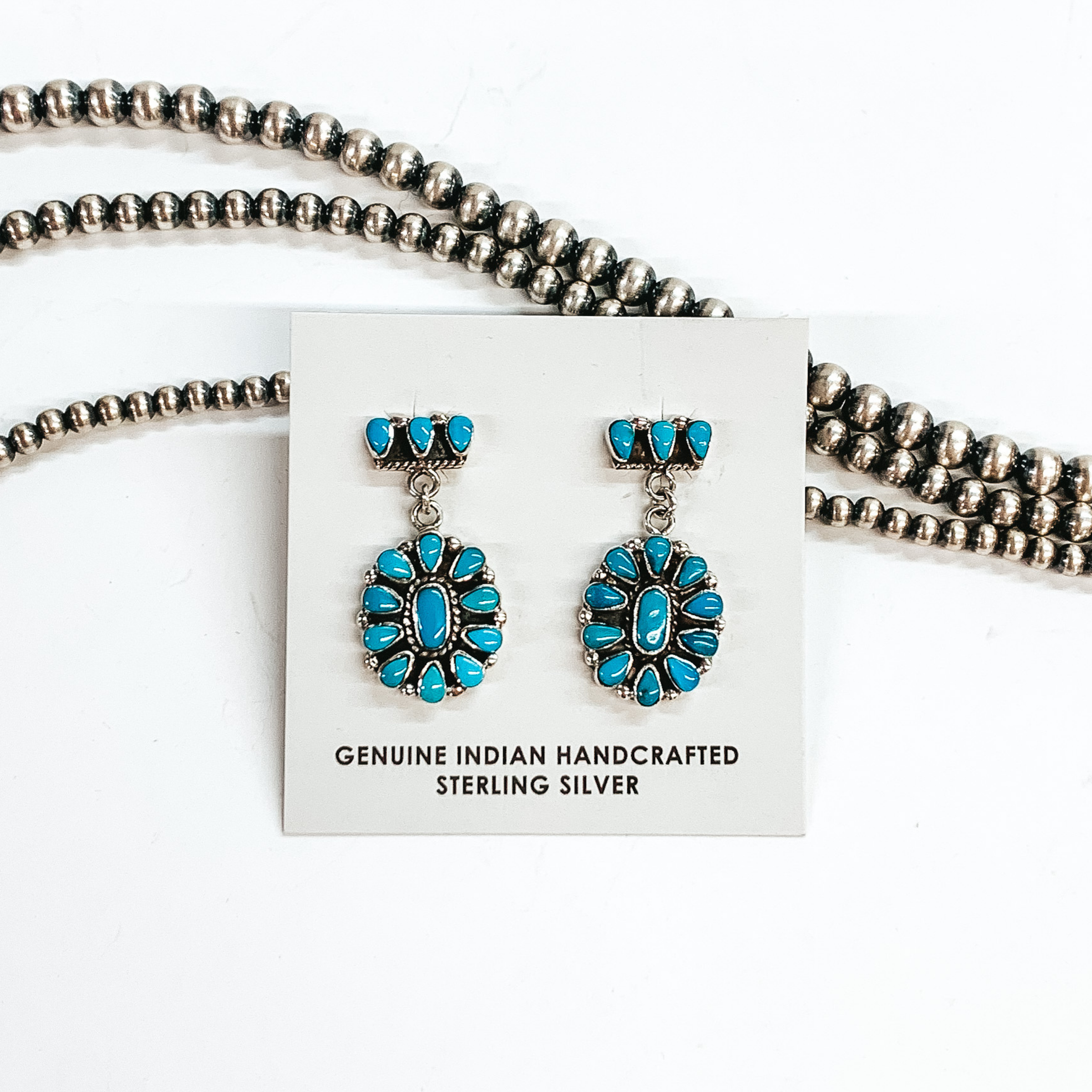 Three turquoise stone post back earrings laid on silver with a turquoise stone cluster laid on silver drop. These earrings are pictured on a white background laying on top of silver beads. 