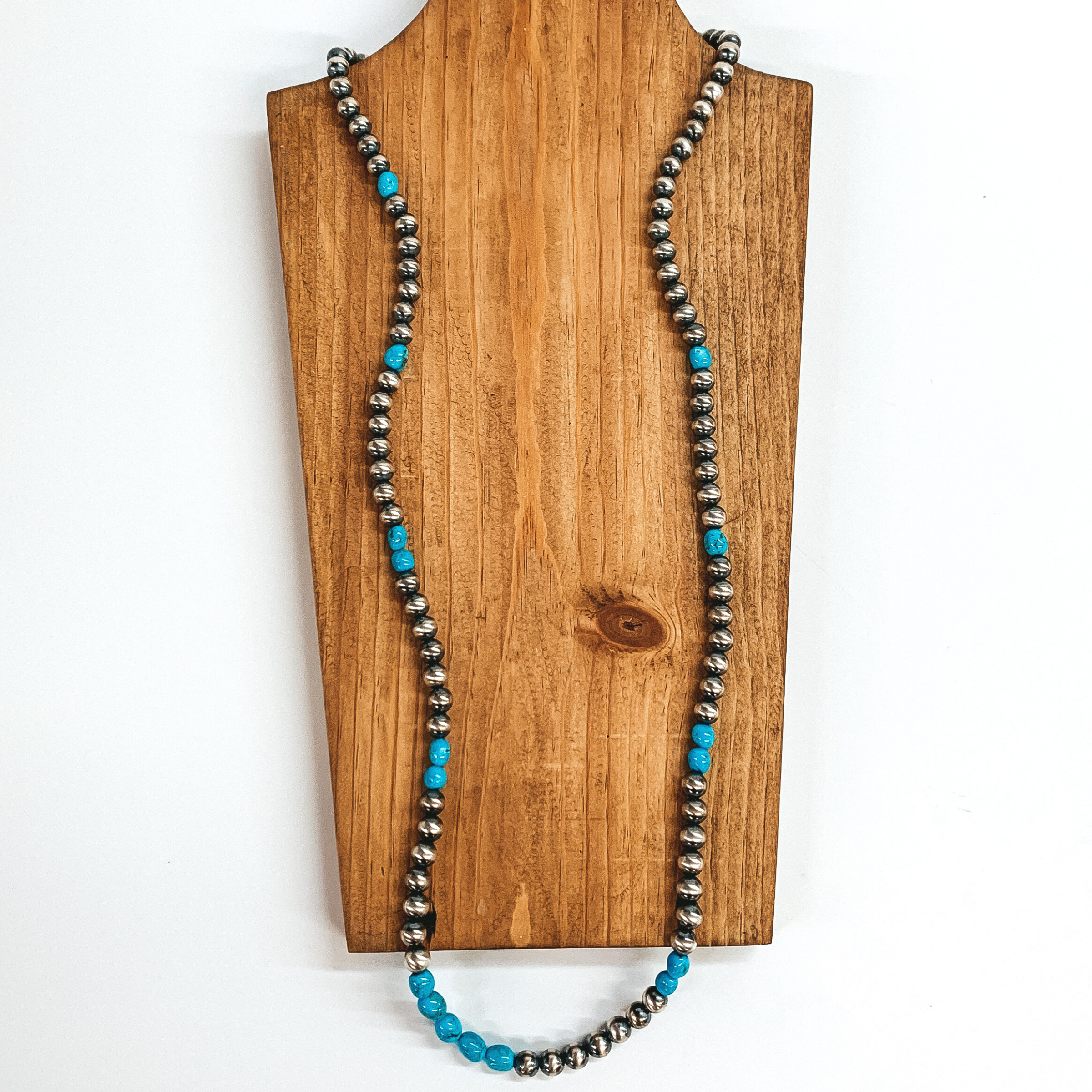 Silver beaded necklace with turquoise beads. This necklace is pictured on a brown necklace holder on a white background. 