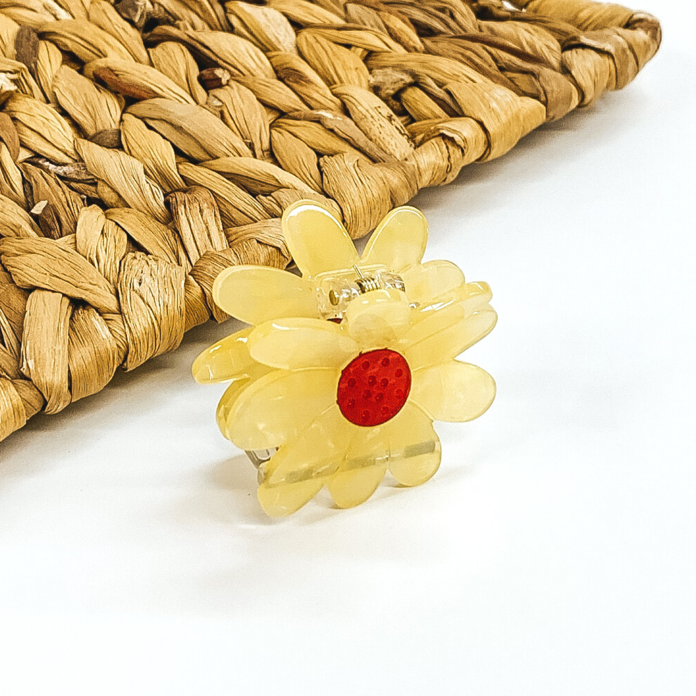 Flower shaped clip in yellow with a red center. This clip is pictured on a white background with a basket weave behind the clip. 