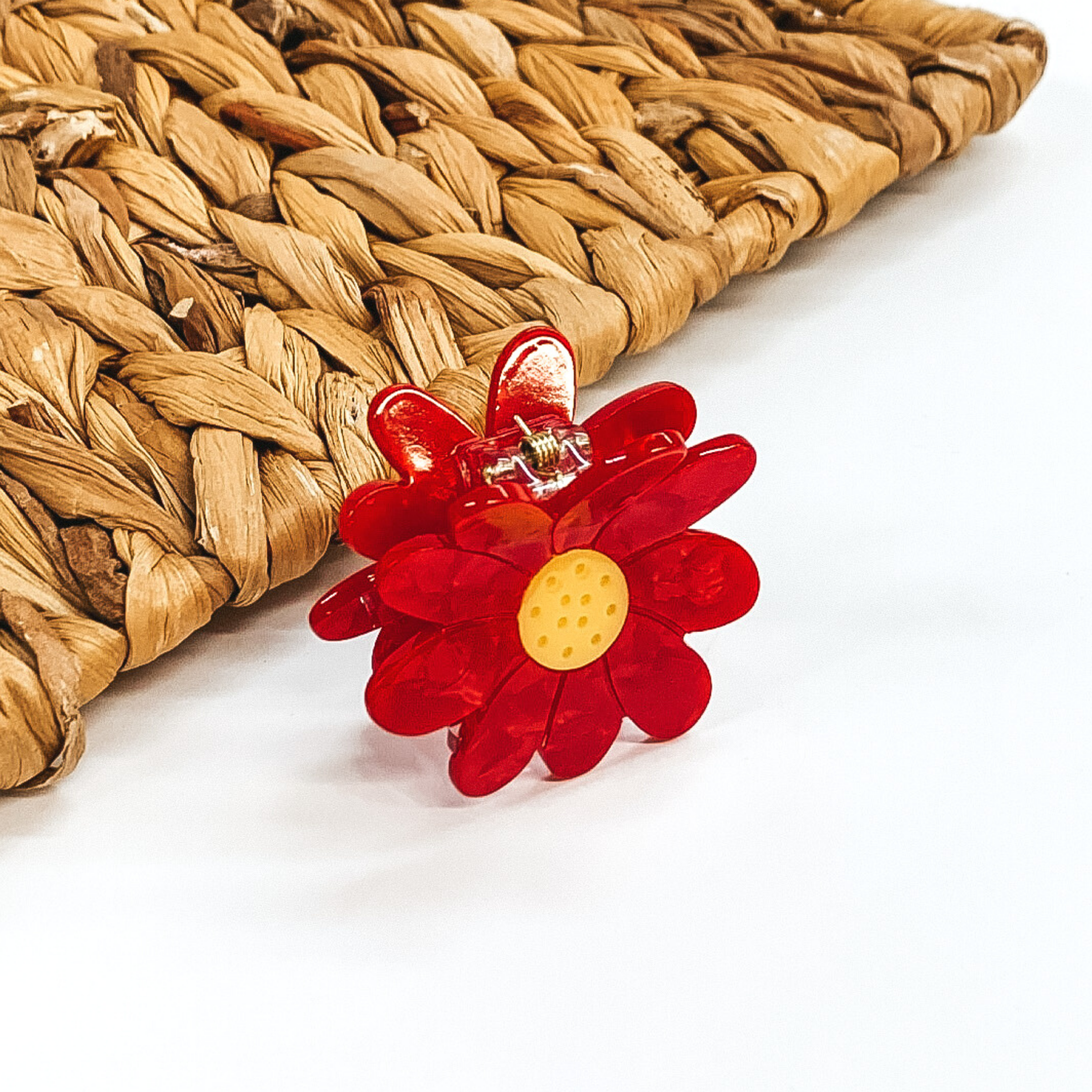 Flower shaped clip in red with a yellow center. This clip is pictured on a white background with a basket weave behind the clip.