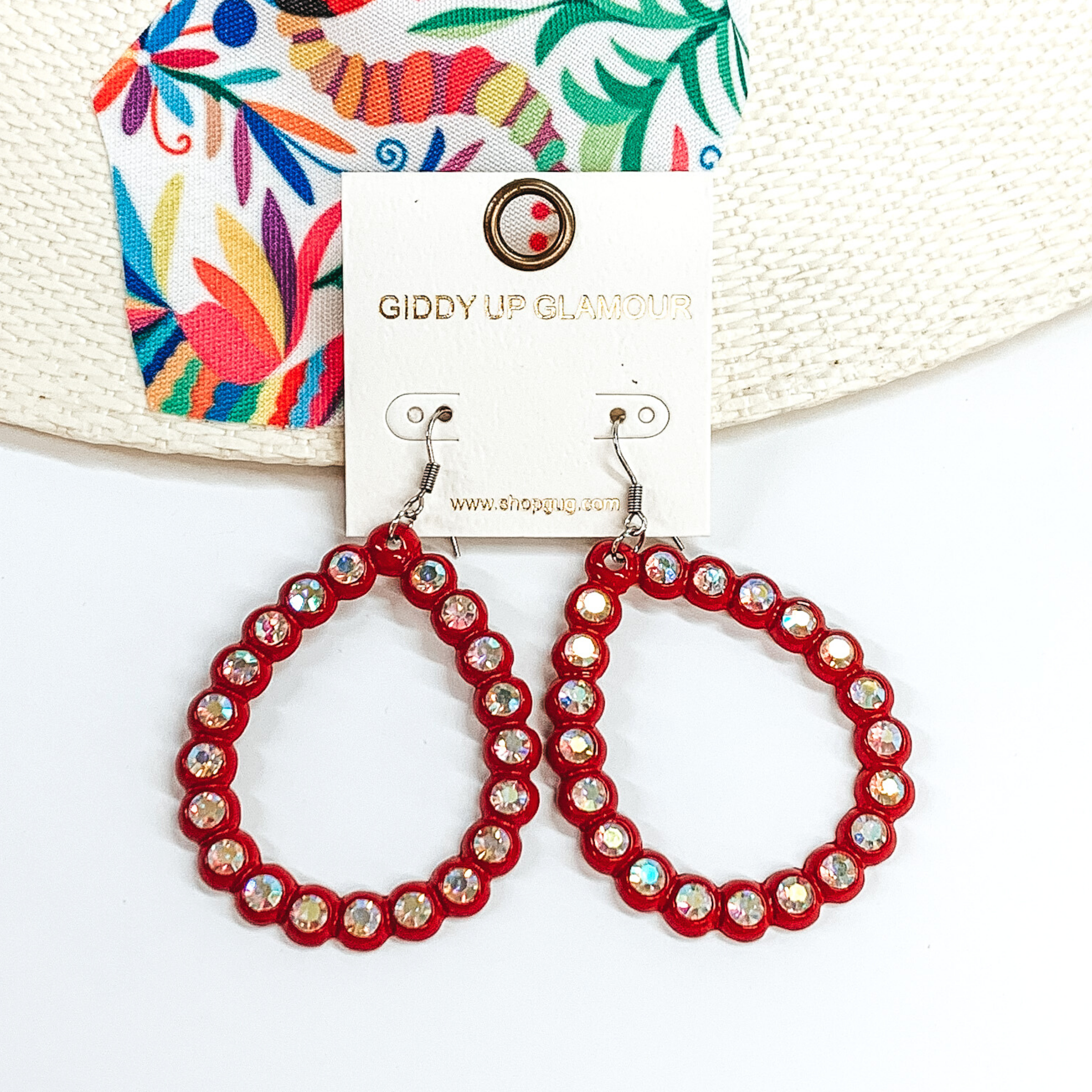 Red, open teardrop earrings with ab crystal outline. These earrings are pictured on a white background with a colorful piece of fabric behind them.