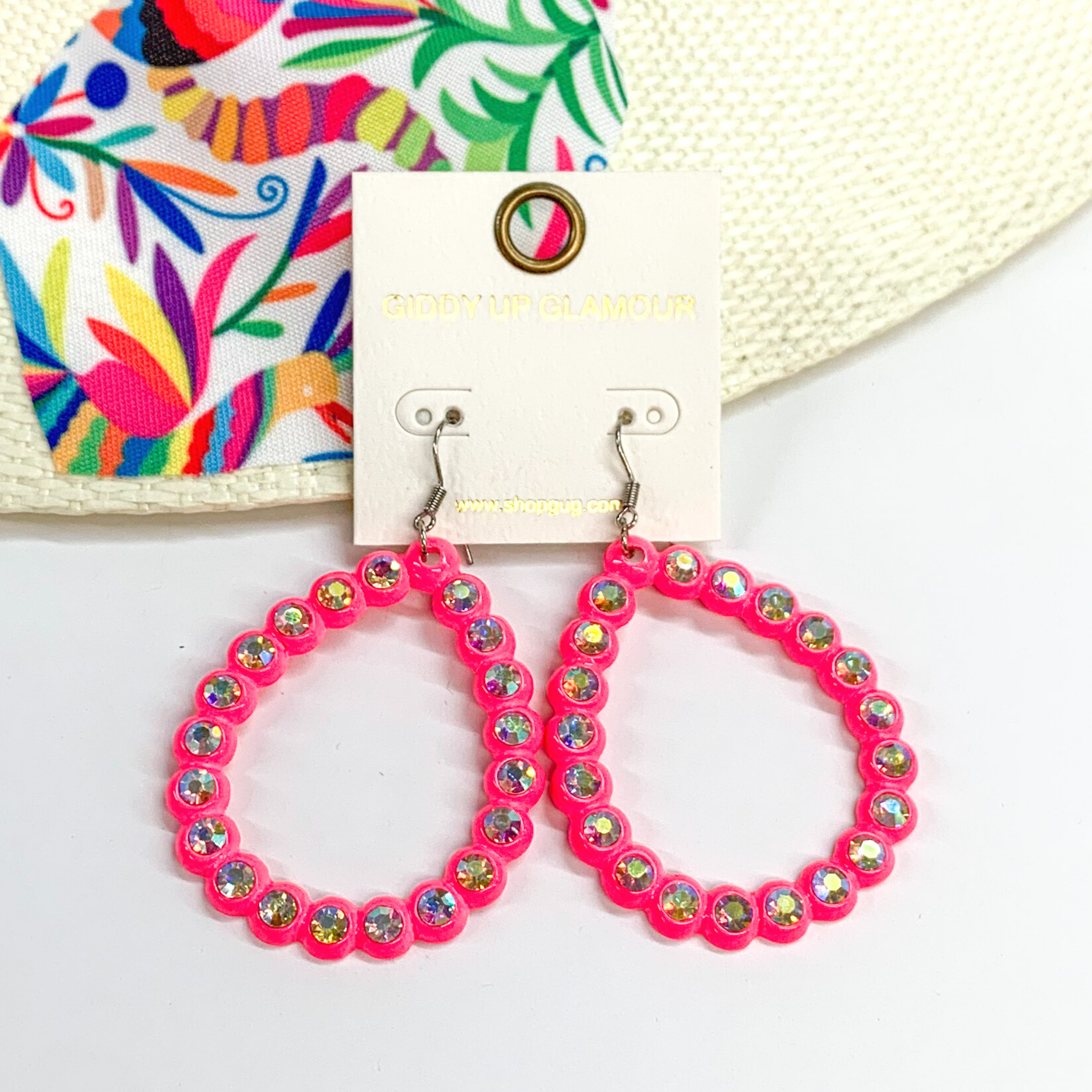 Neon pink, open teardrop earrings with ab crystal outline. These earrings are pictured on a white background with a colorful piece of fabric behind them.