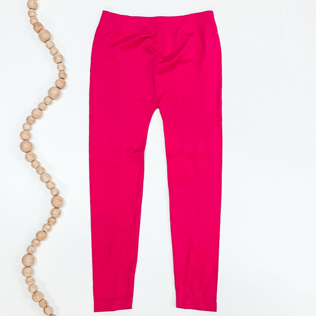 Hot pink colored leggings pictured on a white background with tan beads to the left of the leggings.