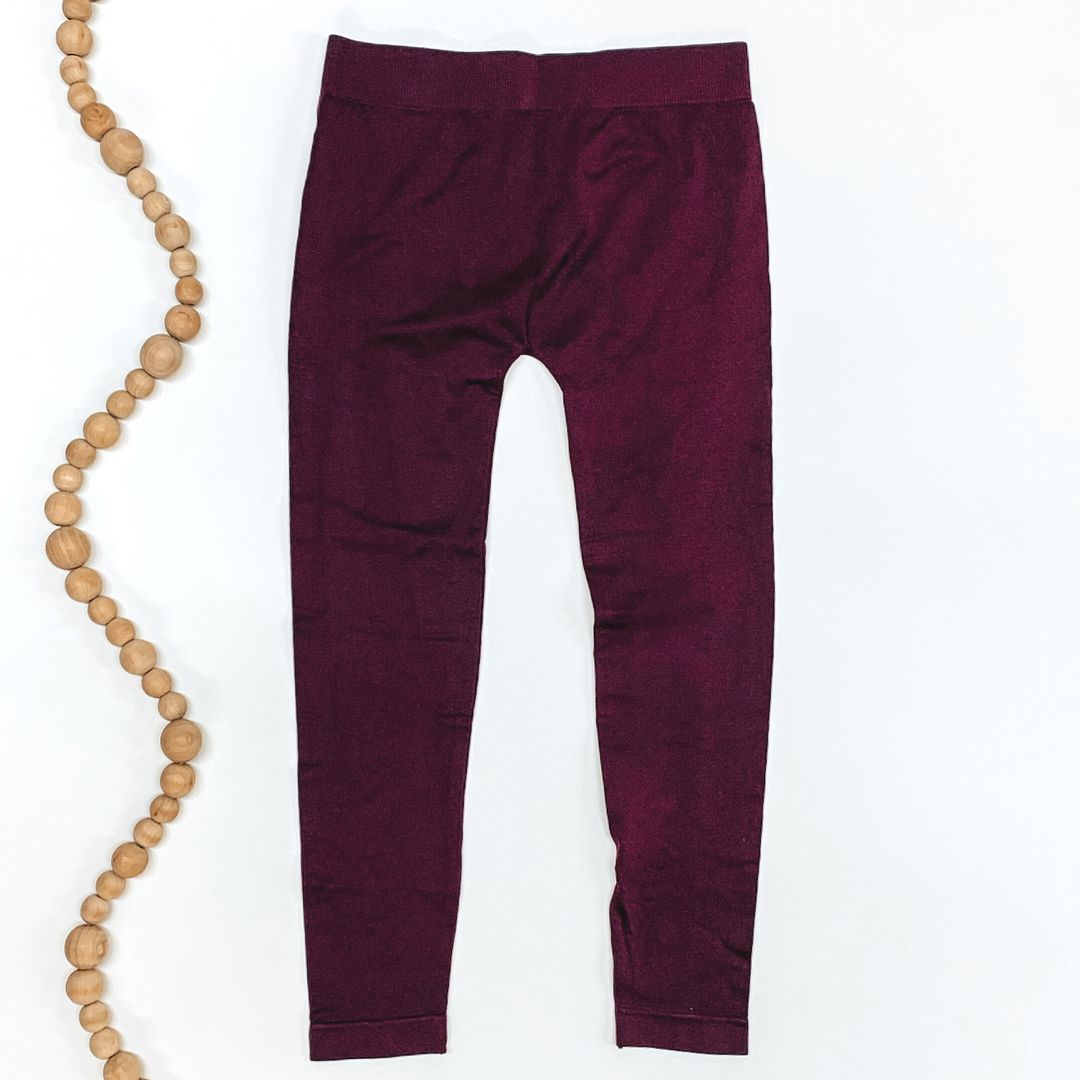 Purple colored leggings pictured on a white background with tan beads to the left of the leggings.