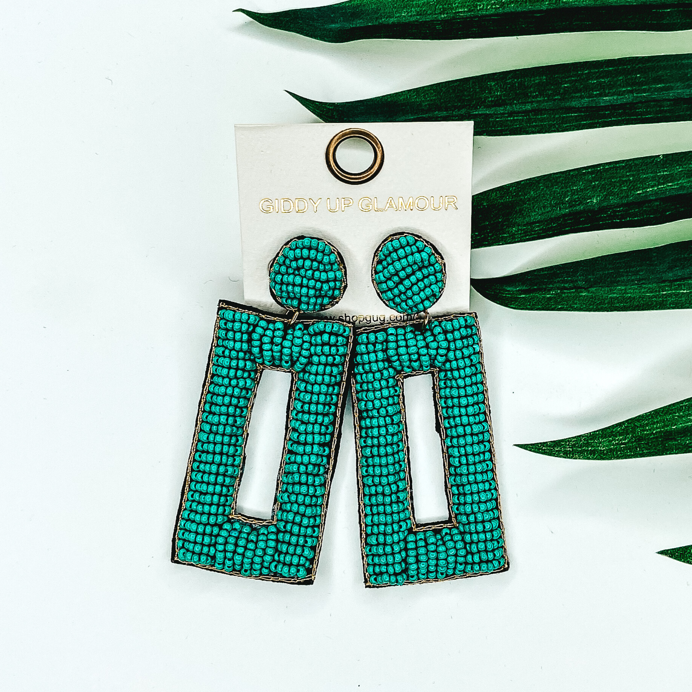 Teal beaded circle post back earrings with a hanging beaded open rectangle pendant. This pair of earrings is pictured on a white background with green leaves behind them.