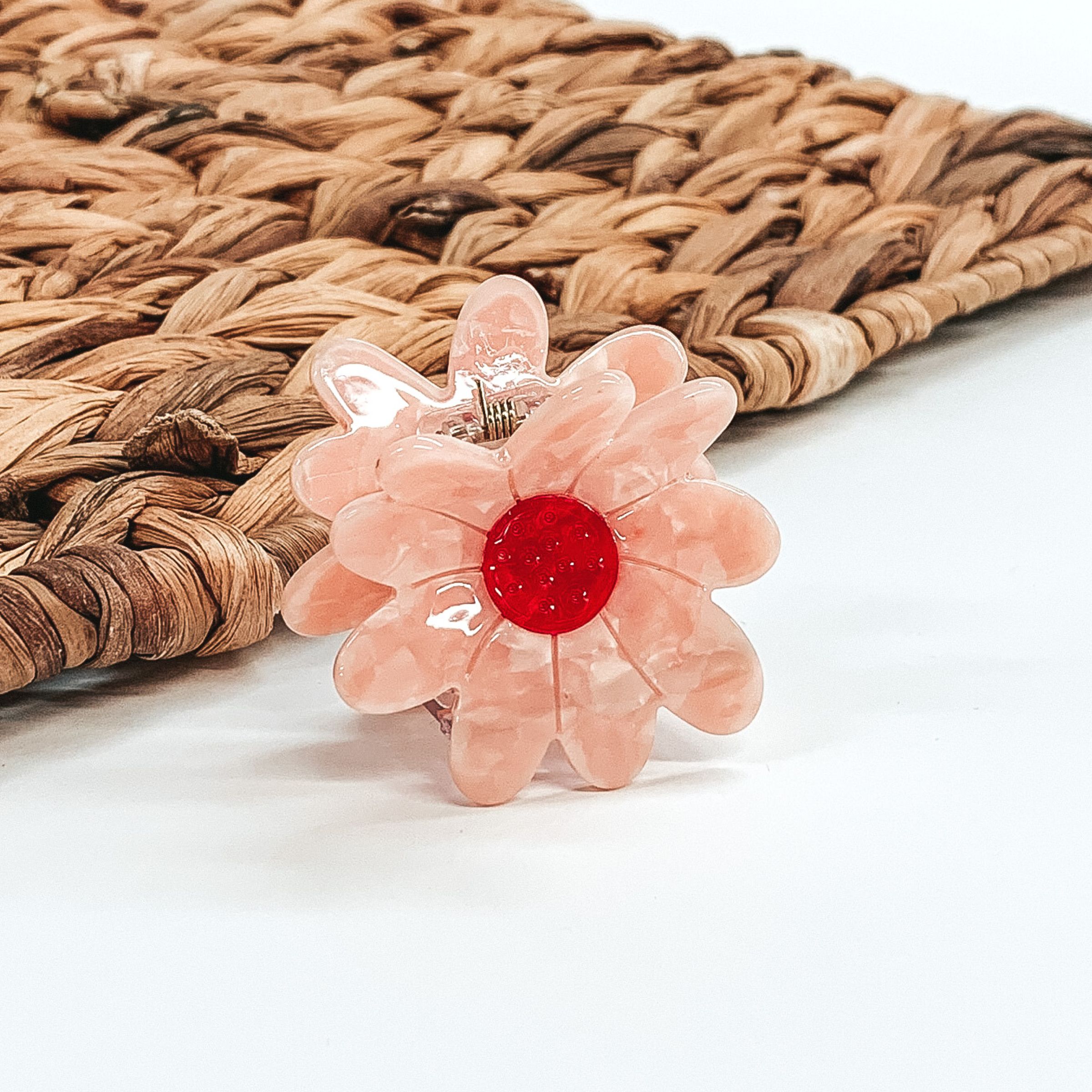 Flower shaped clip in pink with a red center. This clip is pictured on a white background with a basket weave behind the clip.