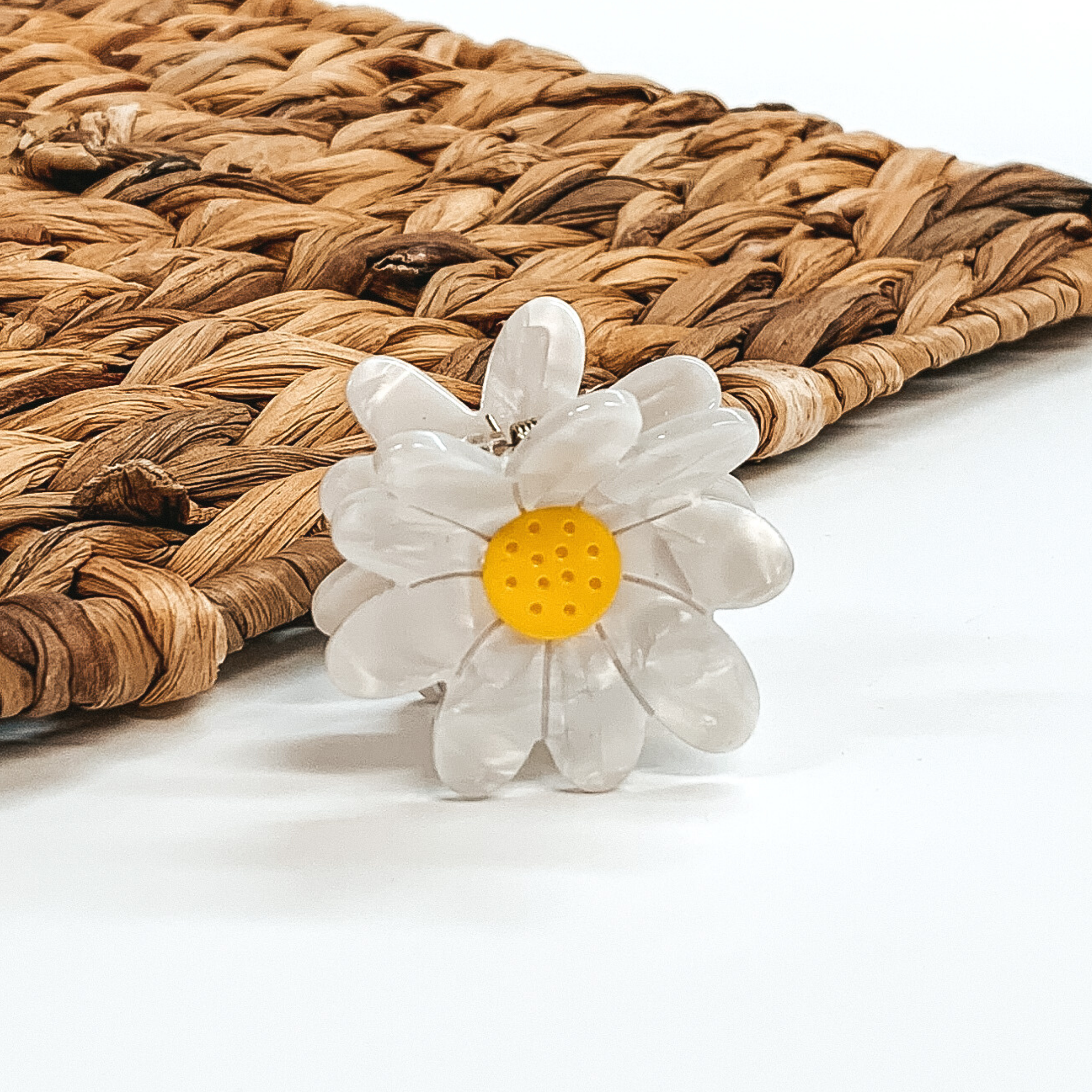 Flower shaped clip in white with a yellow center. This clip is pictured on a white background with a basket weave behind the clip.