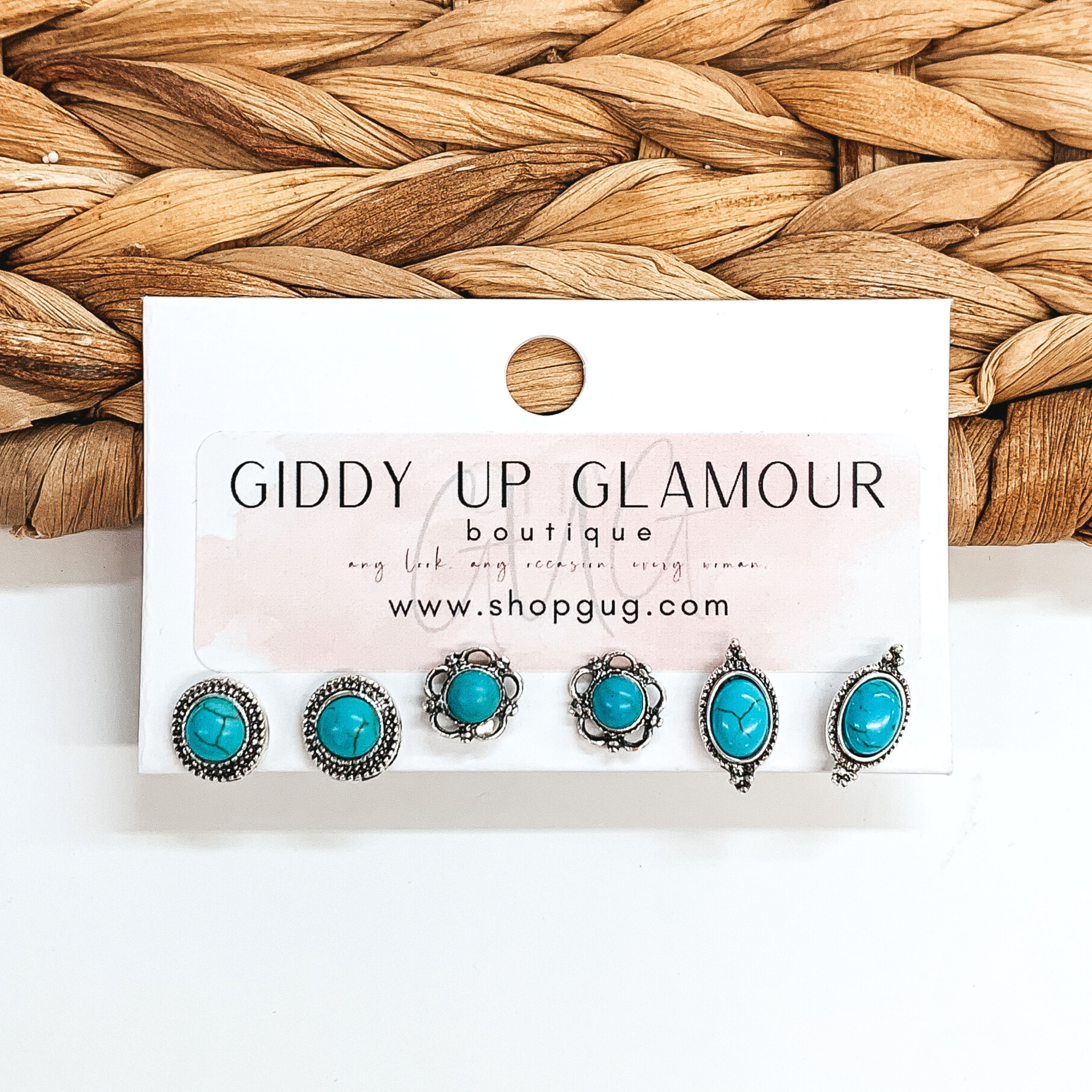 Set of three silver circle and oval stud earrings. All three pairs of earrings include turquoise colored stones with a different silver outline on each pair. These earrings are pictured on a white card holder on a white background with basket weave in the background.