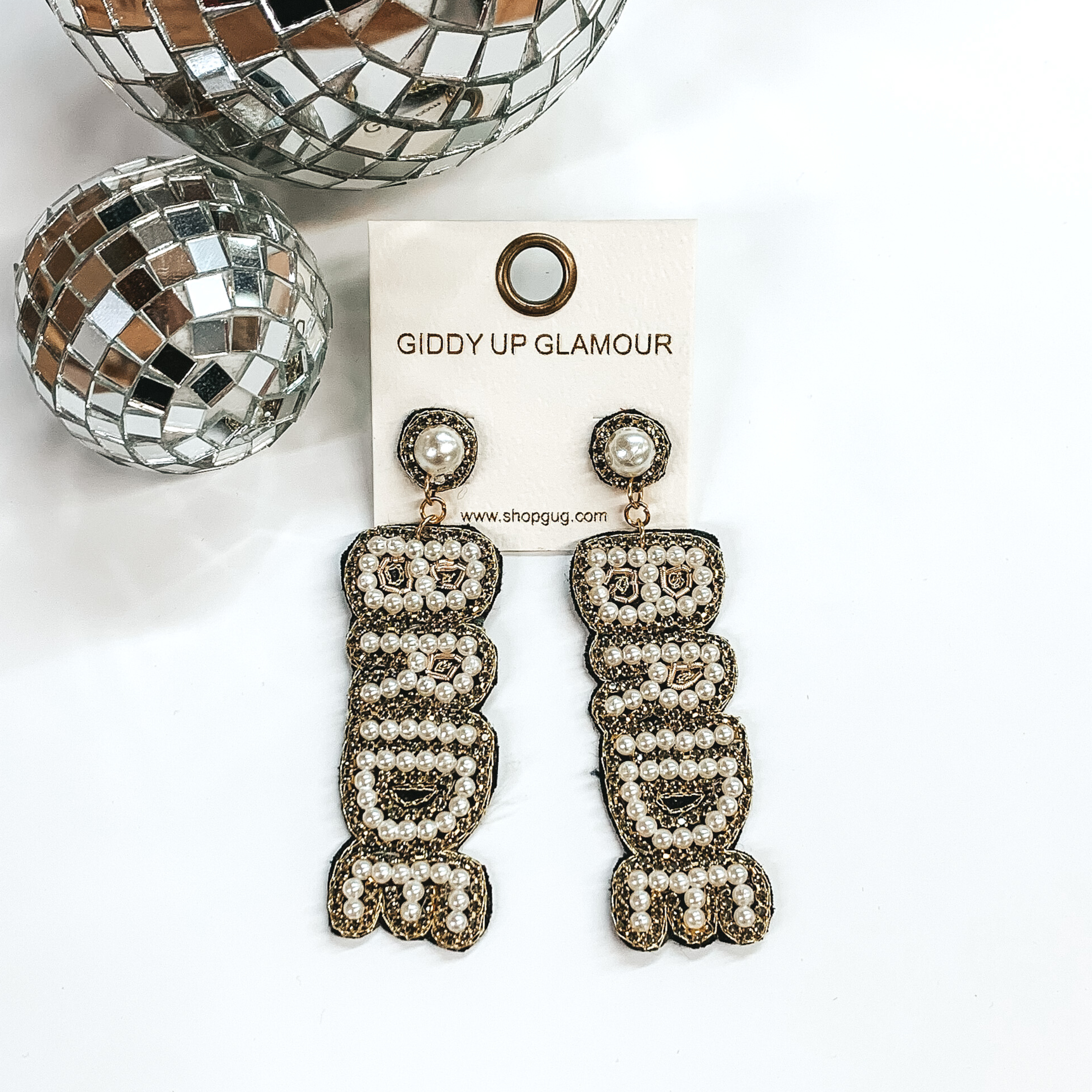 White pearl beaded "BRIDE" drop earrings surrounded by grey crystals and gold stitching. These earrings are pictured on a white background with disco balls in the top left corner.
