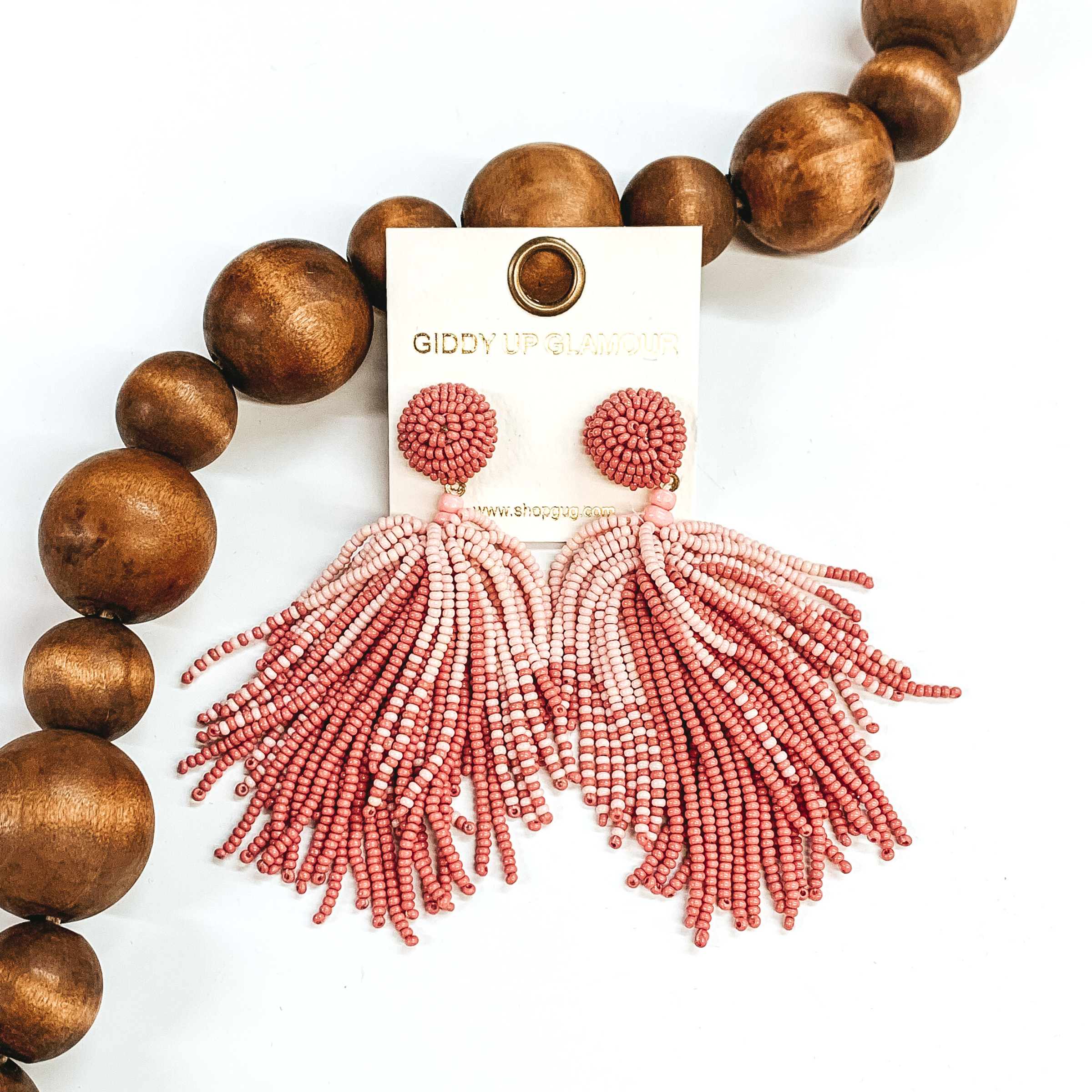 Circle beaded stud earrings with a beaded tassel in dusty pink with baby pink tops. These earrings are pictured on a white background with brown beads behind them. 