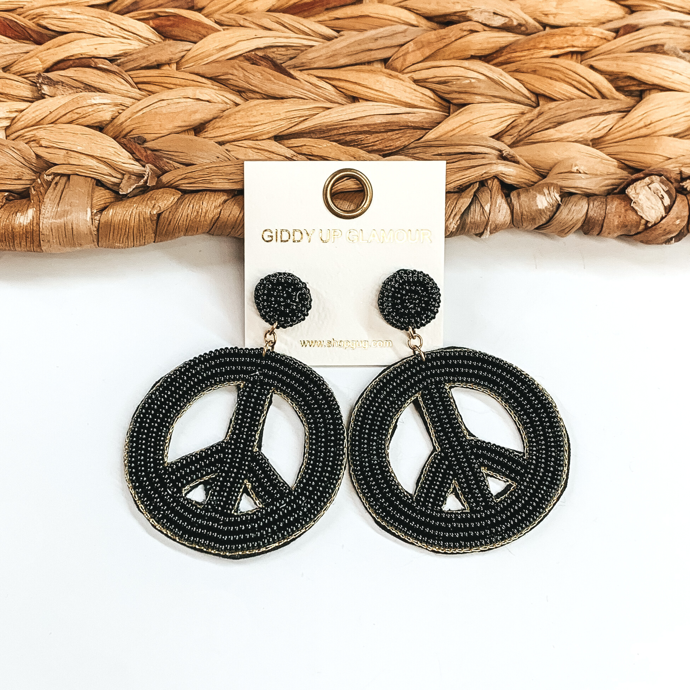 Circle beaded stud earrings with a beaded peace sign in black. These earrings are pictured on a half white and half basket weave background. 