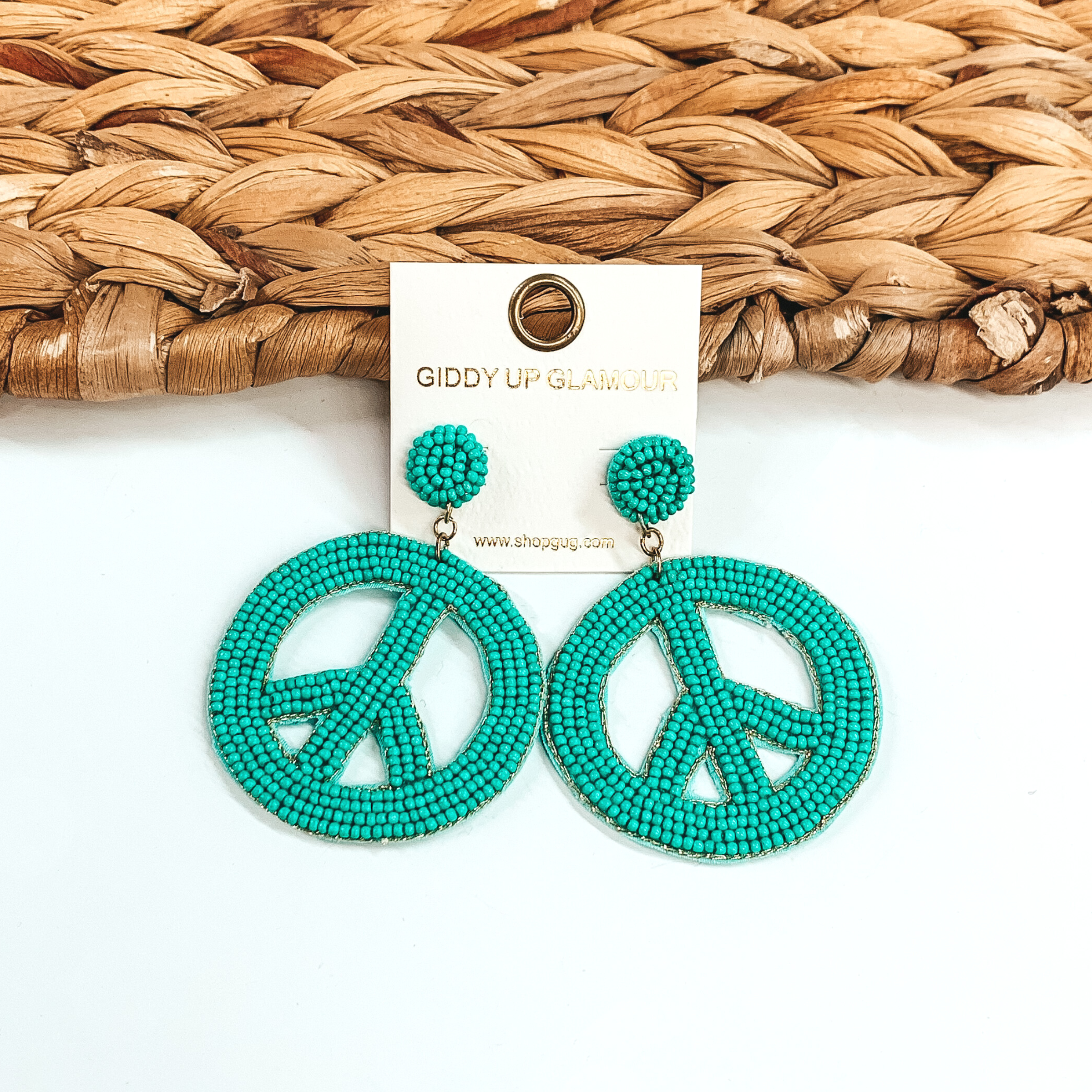 Circle beaded stud earrings with a beaded peace sign in turquoise. These earrings are pictured on a half white and half basket weave background.