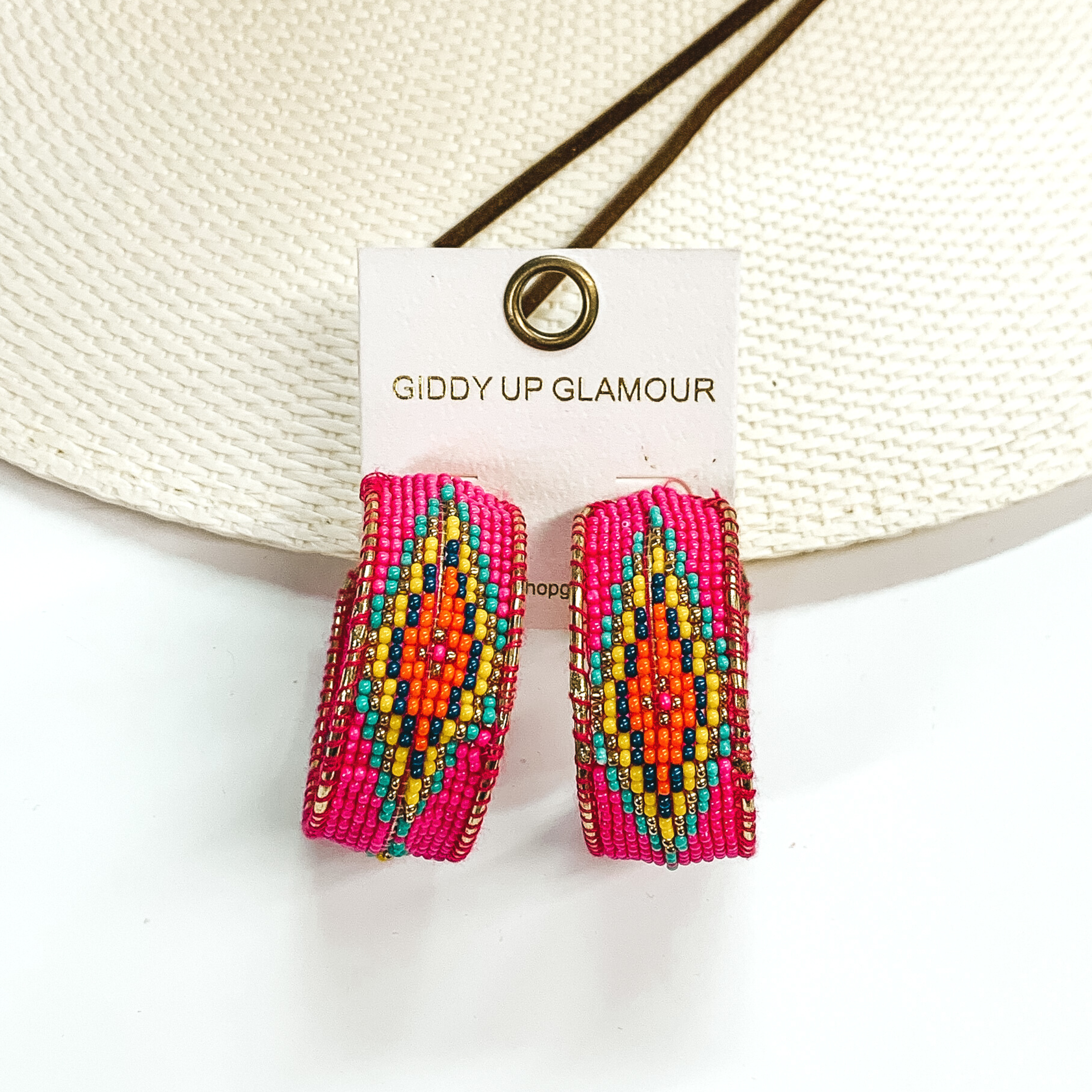Beaded hoop earrings in hot pink with an aztec design in multicolor. These earrings are pictured on a white background on a straw hat. 
