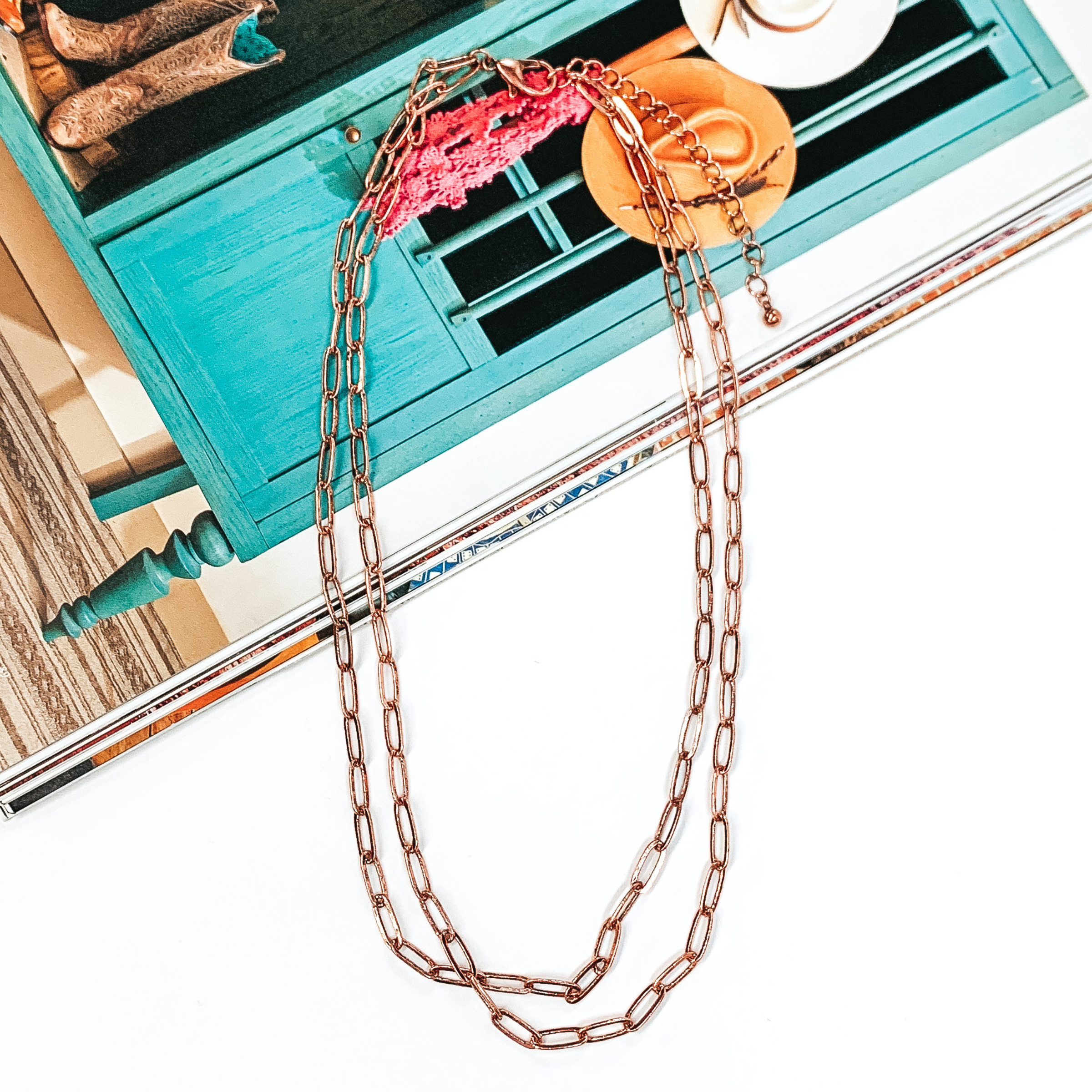 Copper layered paperclip chain necklace that is pictured half on a magazine and half on a white background.