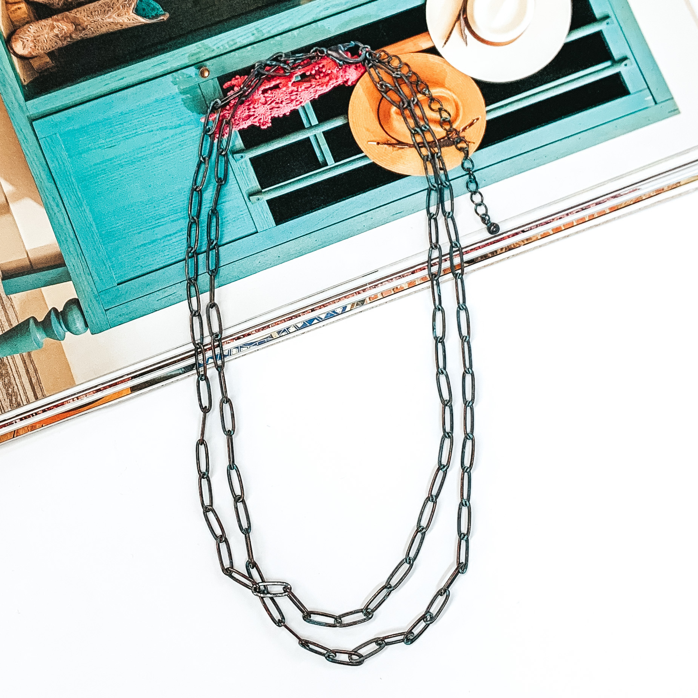 Patina layered paperclip chain necklace that is pictured half on a magazine and half on a white background.