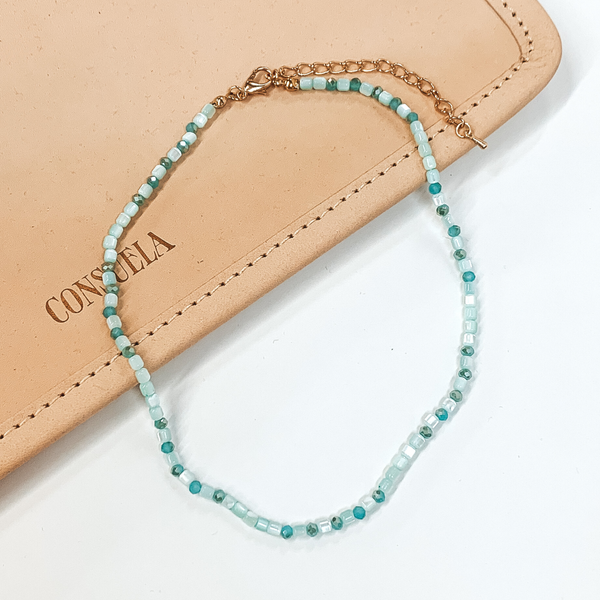 Aqua beaded necklace that is pictured on a white and tan background.